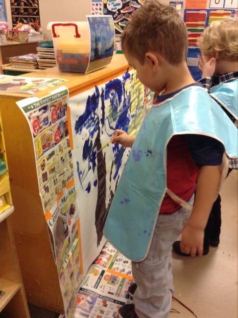Child in a smock painting on a large sheet of paper