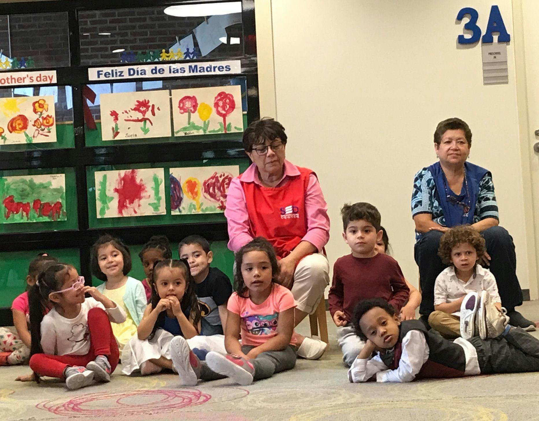 Two adults with a group of children sitting on the floor in a classroom