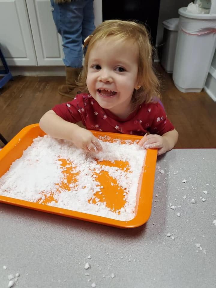 Child playing with white powder in an orange tray