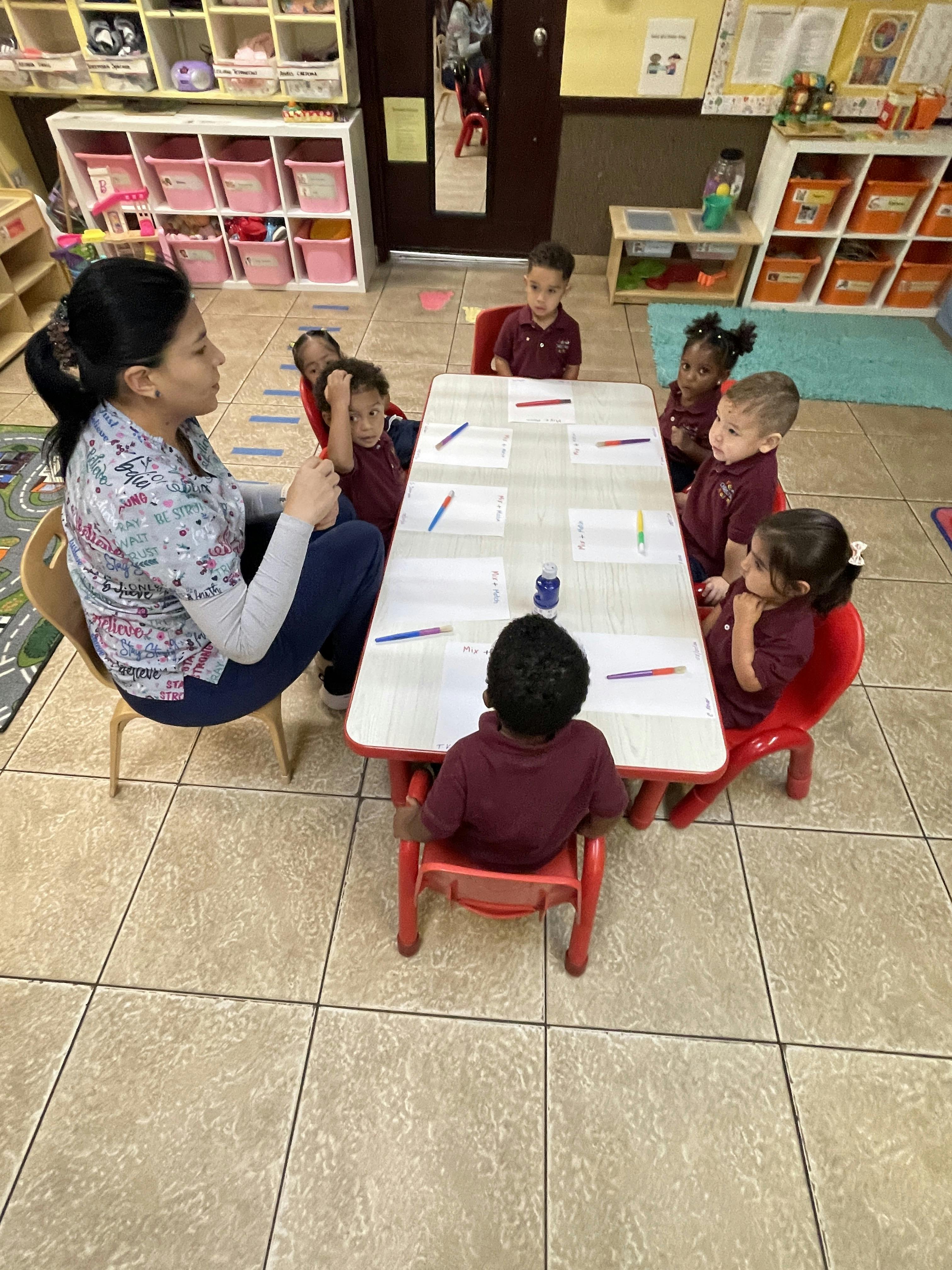 A person sitting at a table with several children in a classroom