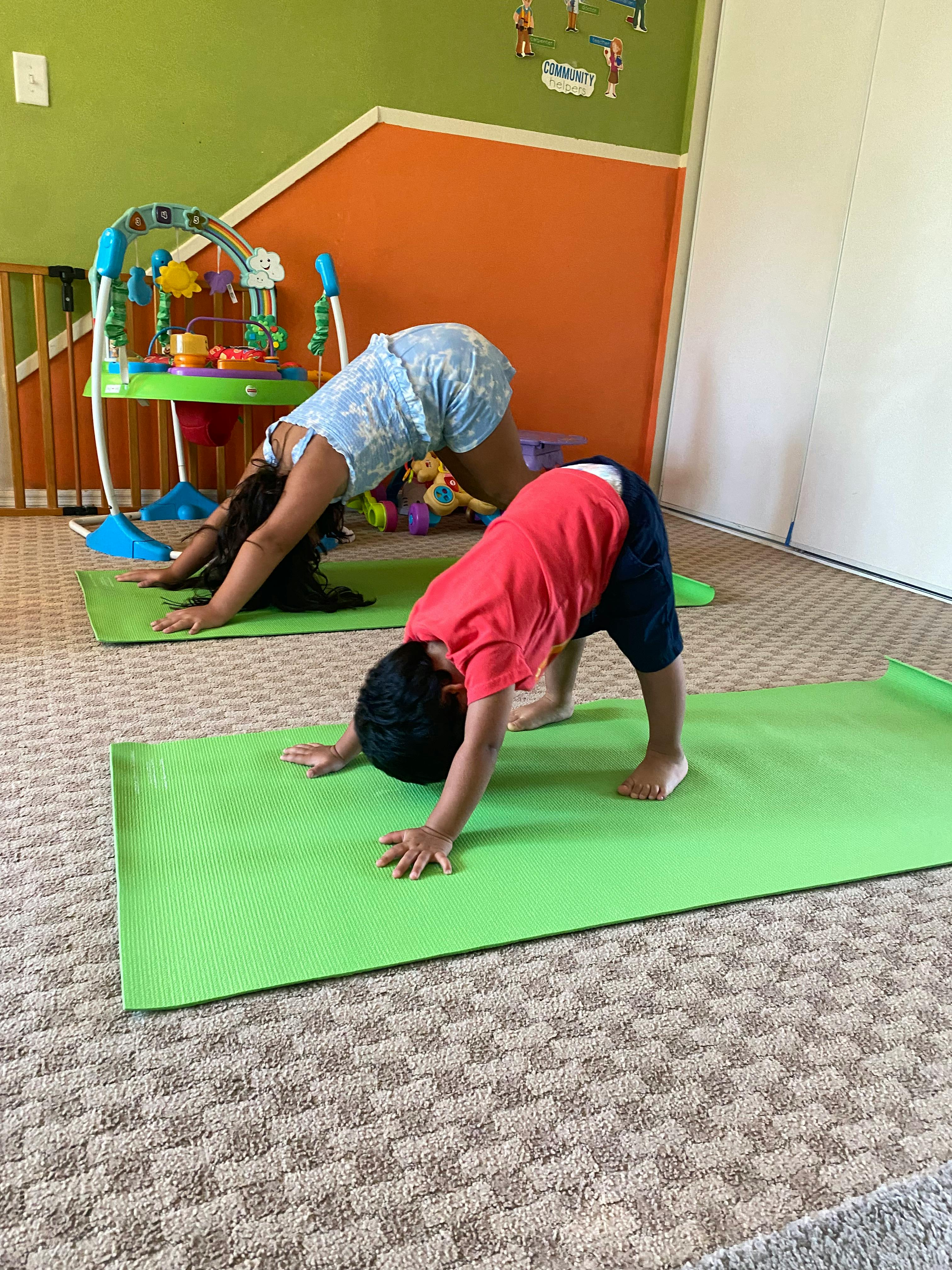 Two children in downward dog yoga pose on green mats