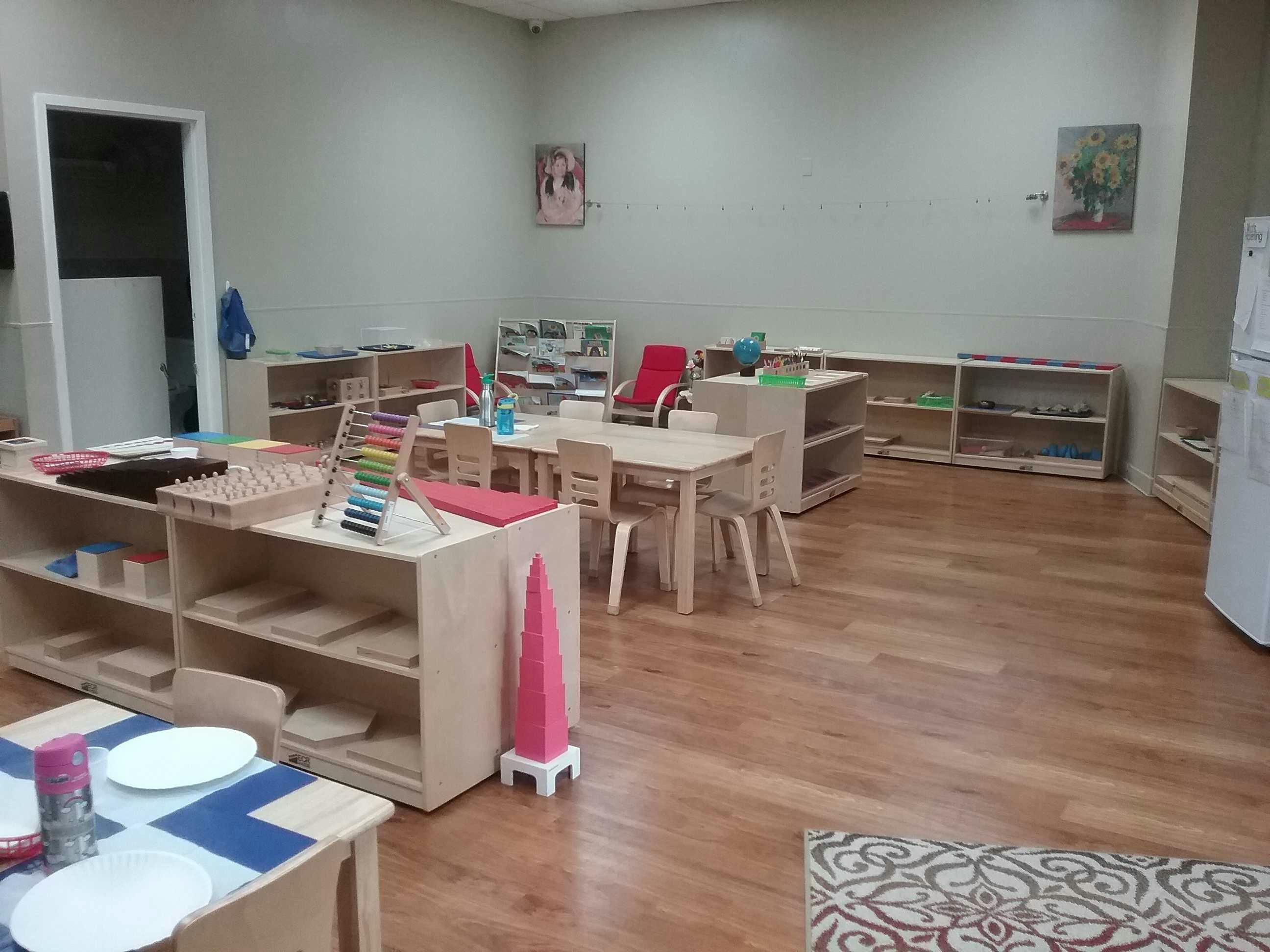 Classroom with small tables and chairs, shelves with learning materials