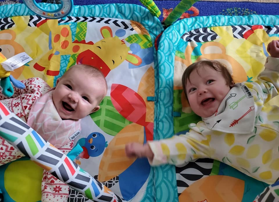 Two babies lying on colorful play mats