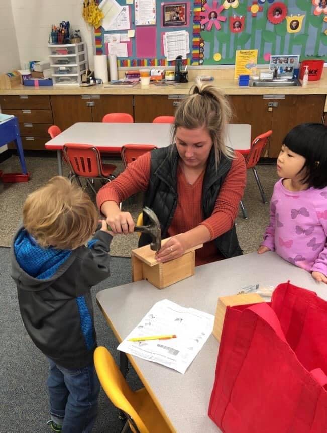 Adult and two children building a wooden birdhouse in a classroom