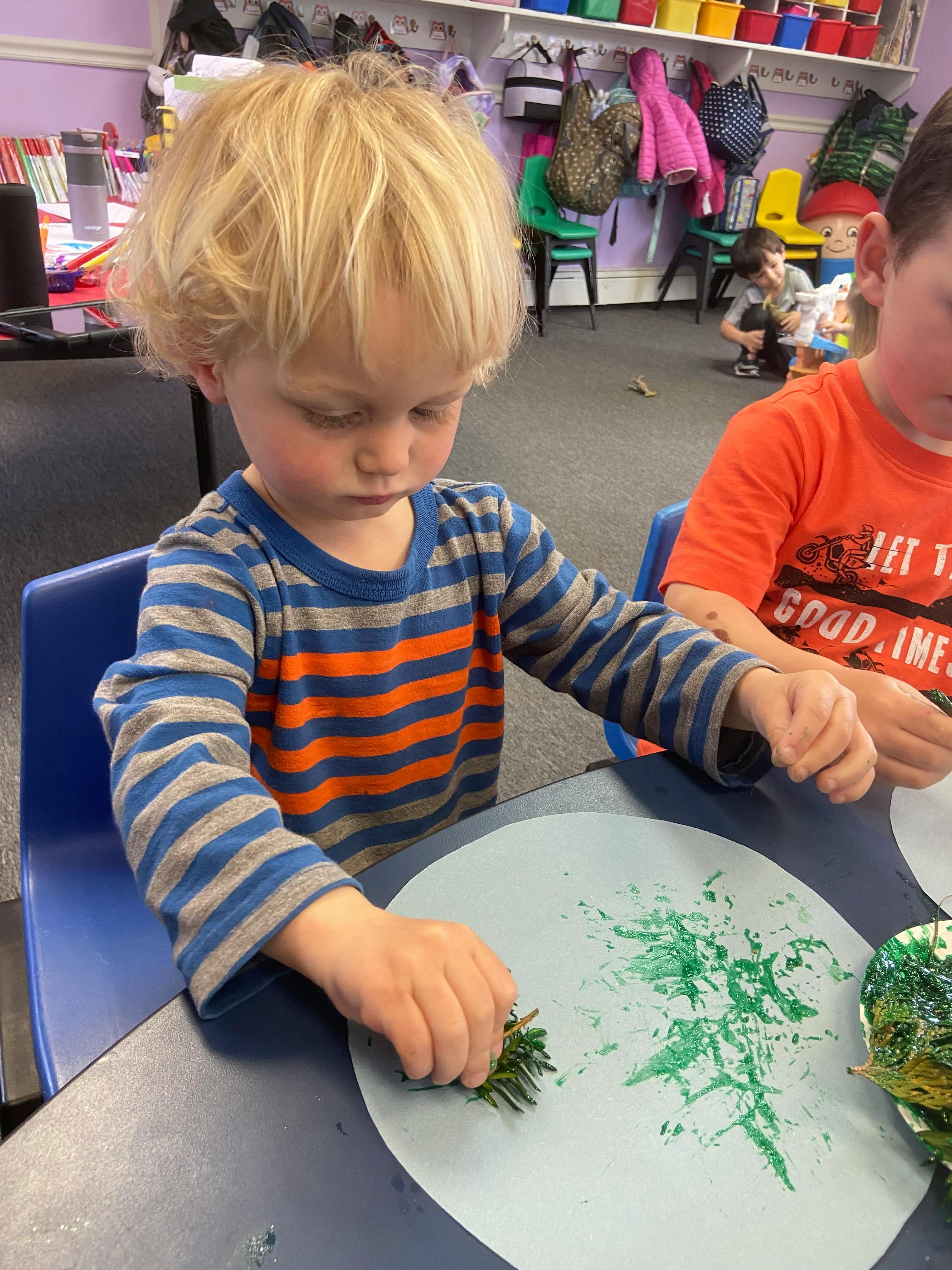 Child making art with a pine branch and green paint