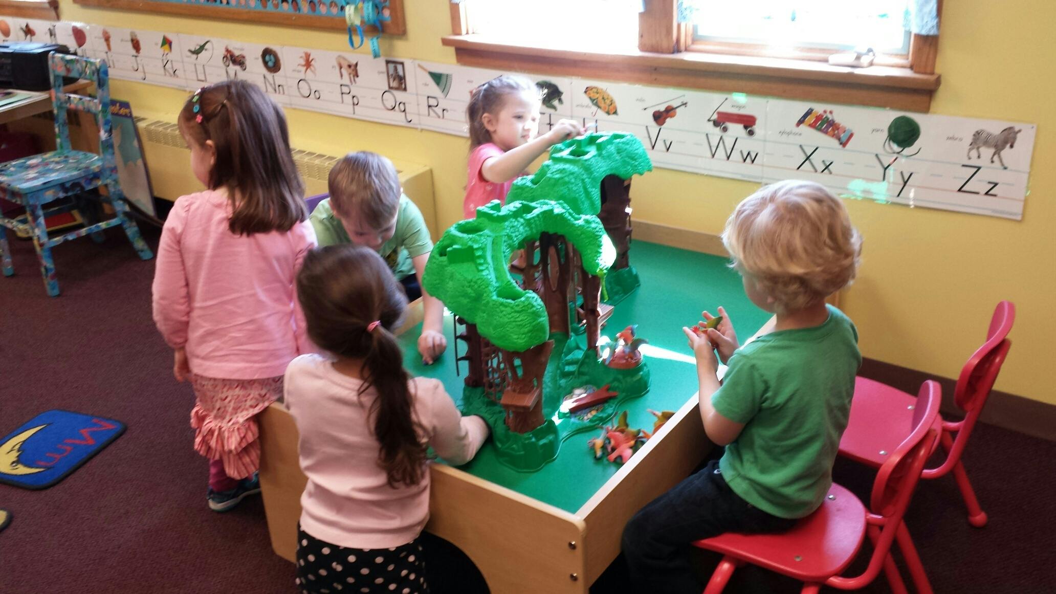 Children playing at a table with a green toy