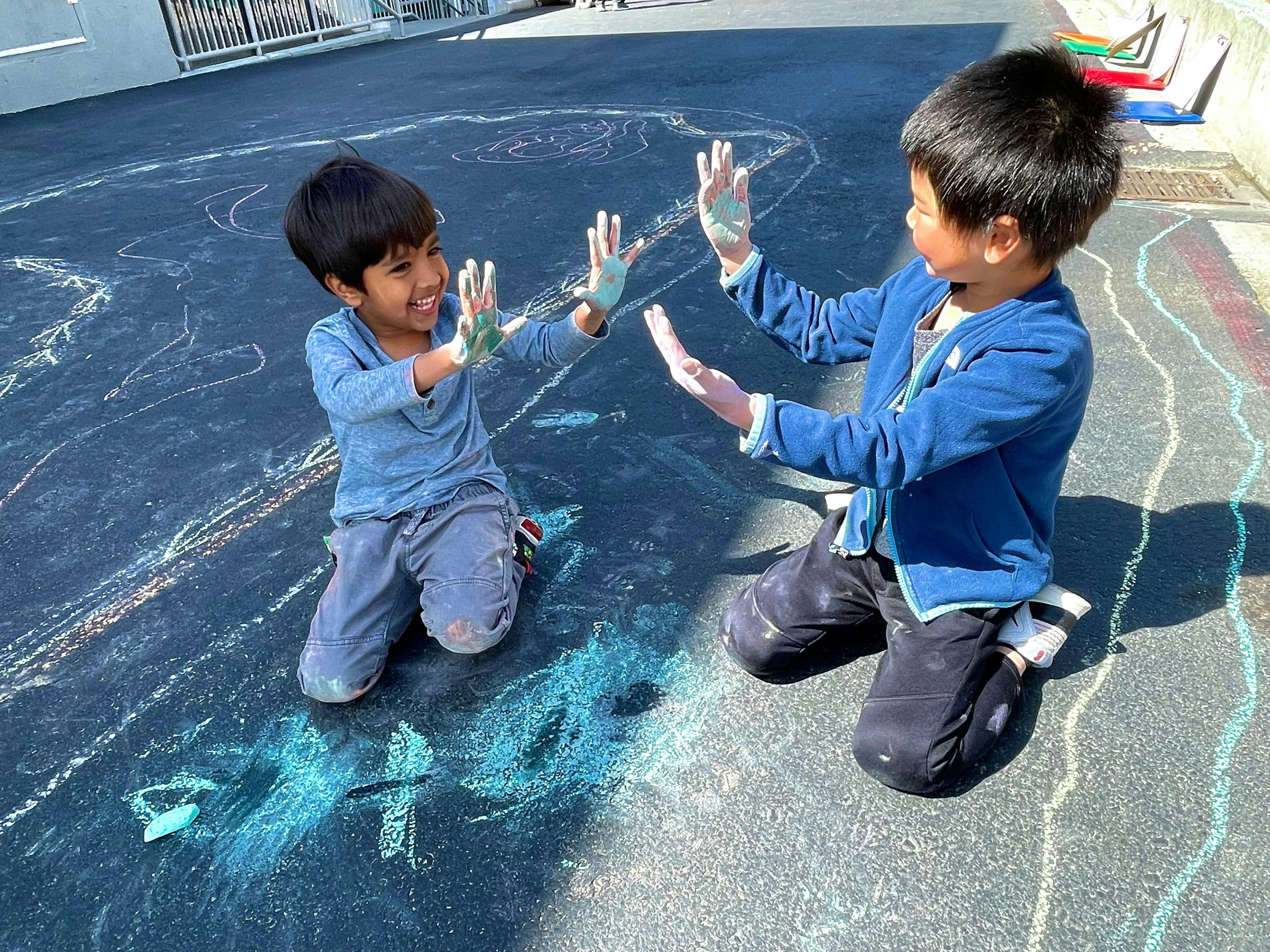Two children kneeling on pavement with chalk on their hands