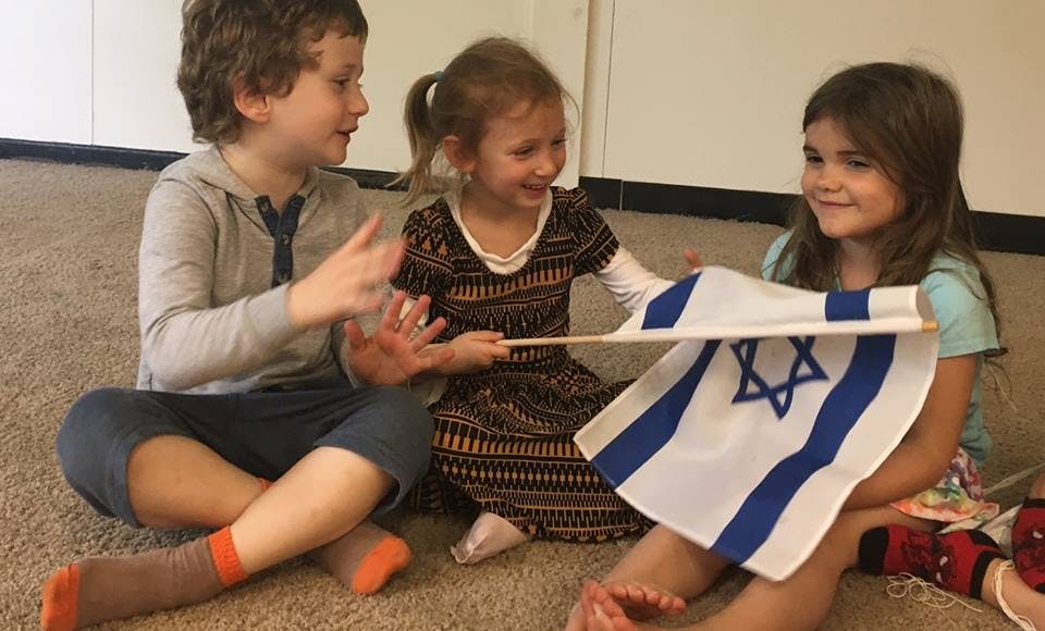 Three children sitting on the floor holding a small flag