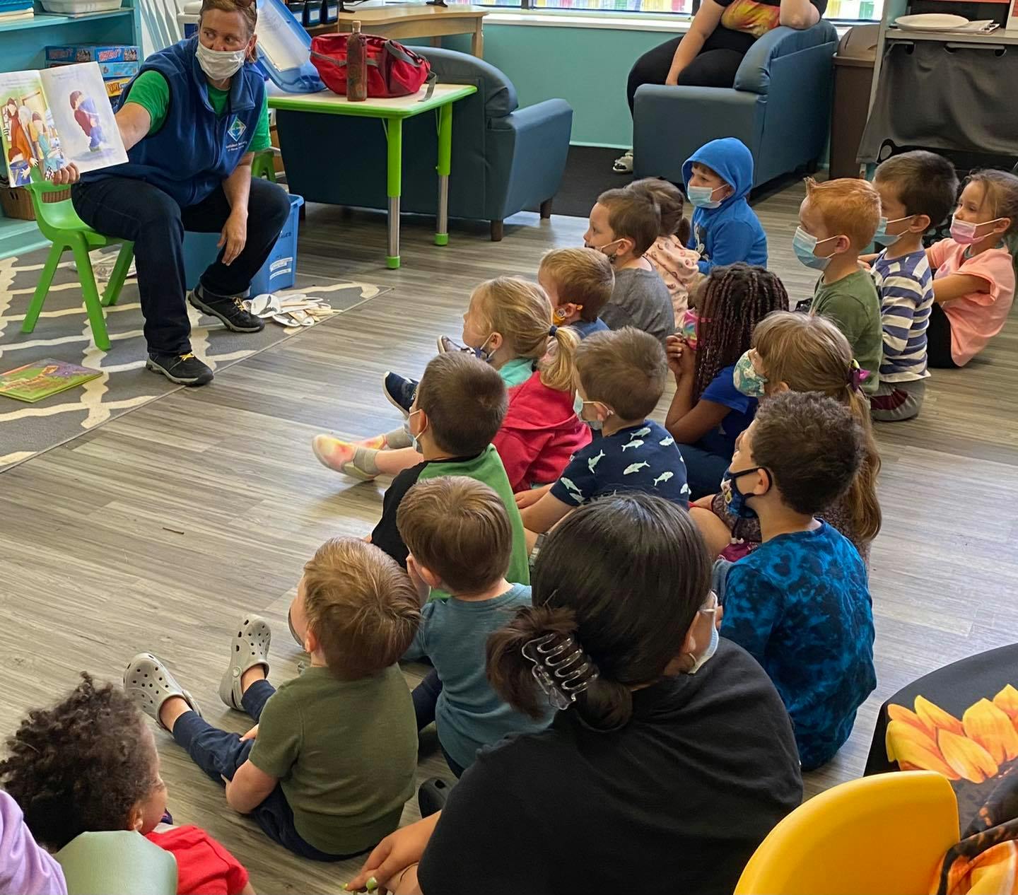 Person reading a book to a group of children sitting children