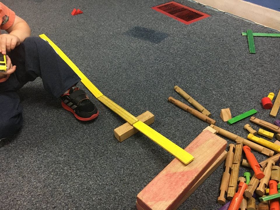 Child playing with wooden blocks and a yellow ramp on a carpeted floor
