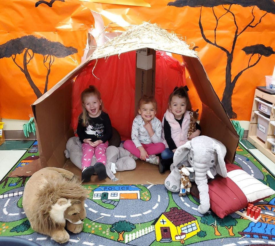 Three children sitting in a play tent with stuffed animals