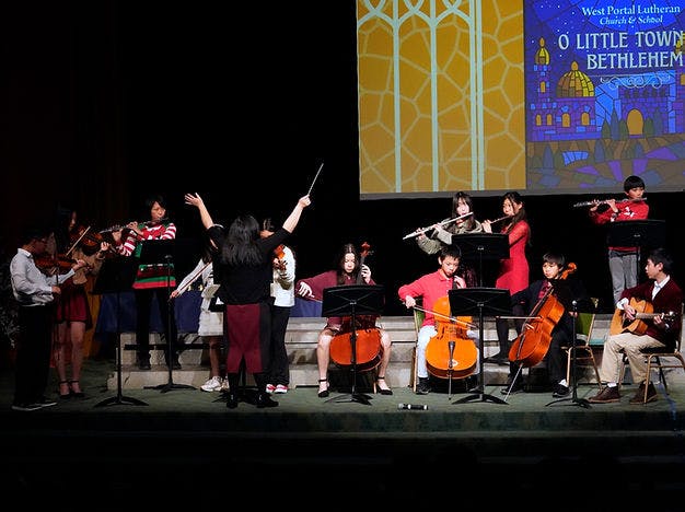Children and a conductor performing with an orchestra on a stage