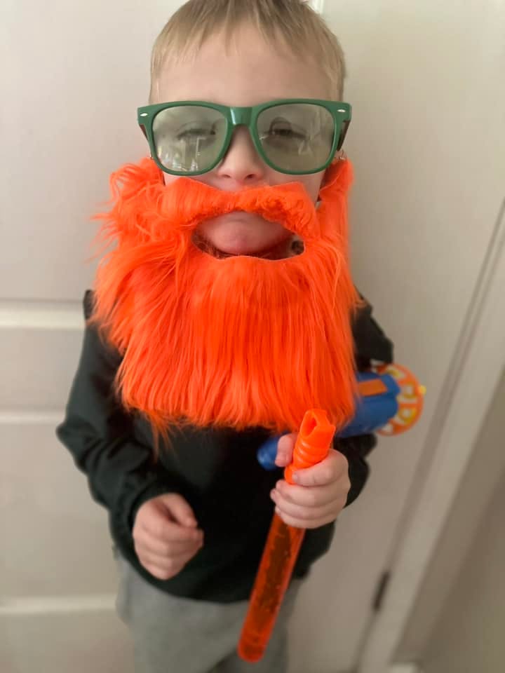 Child wearing green glasses and an orange fake beard, holding a toy