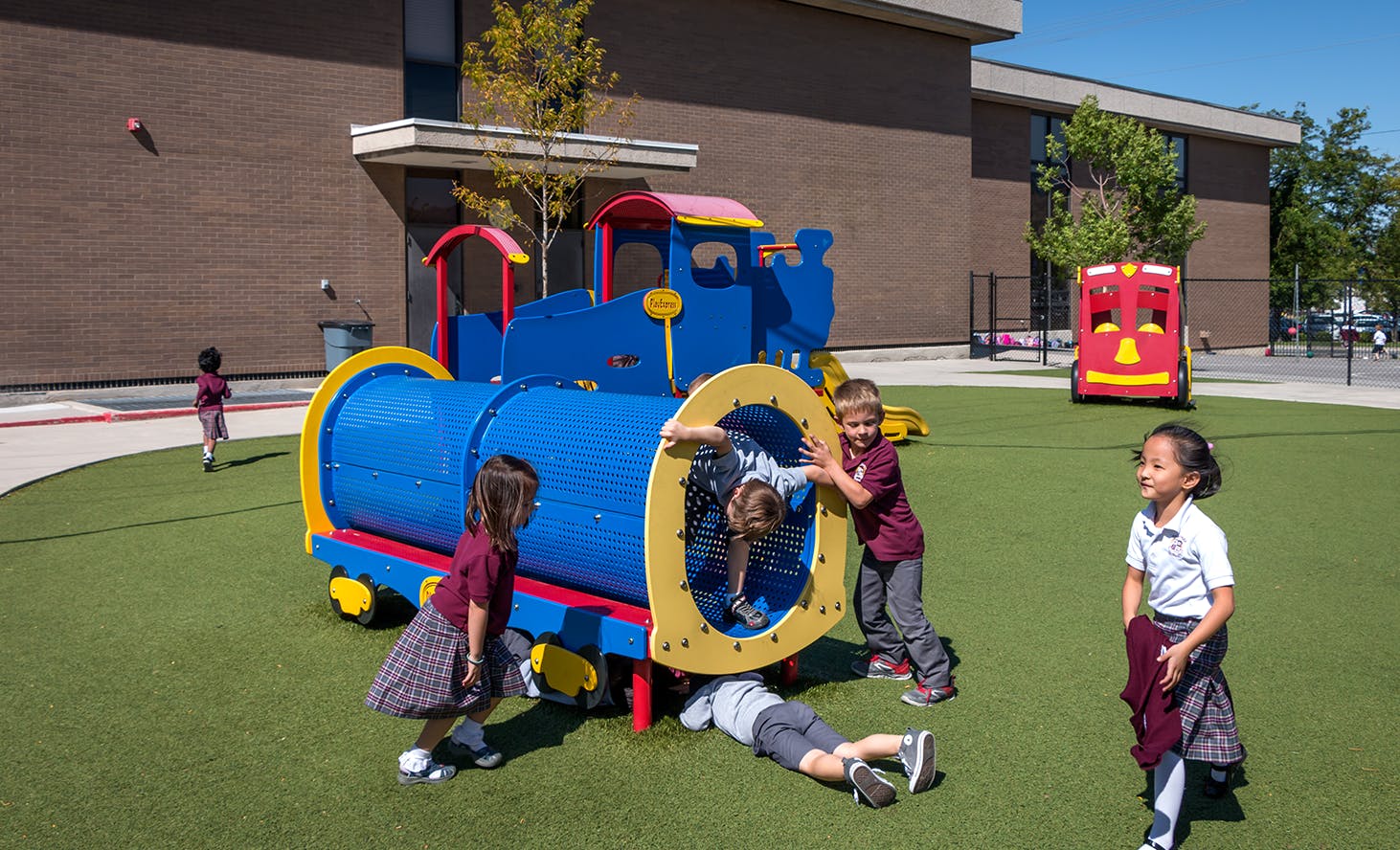 Children playing on and around a blue train-shaped playground structure