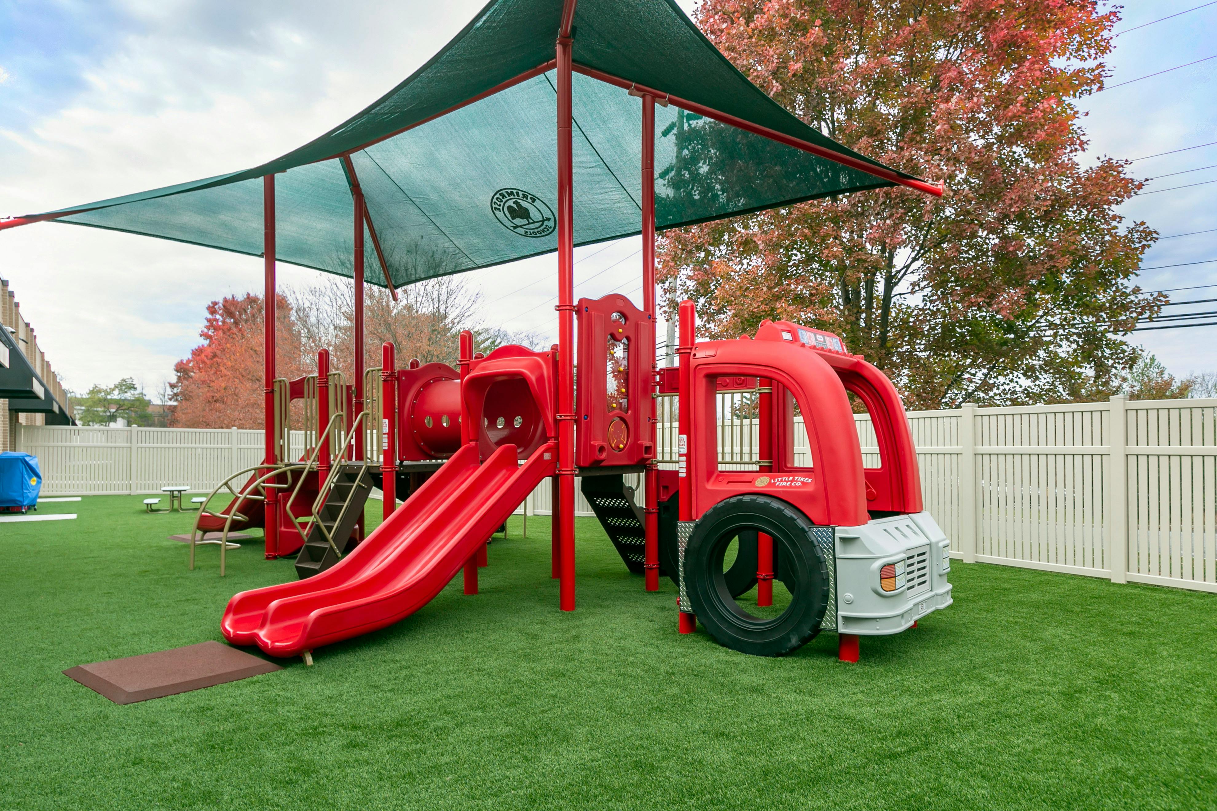 Red playground with slides, tunnels, and a fire truck feature on artificial grass