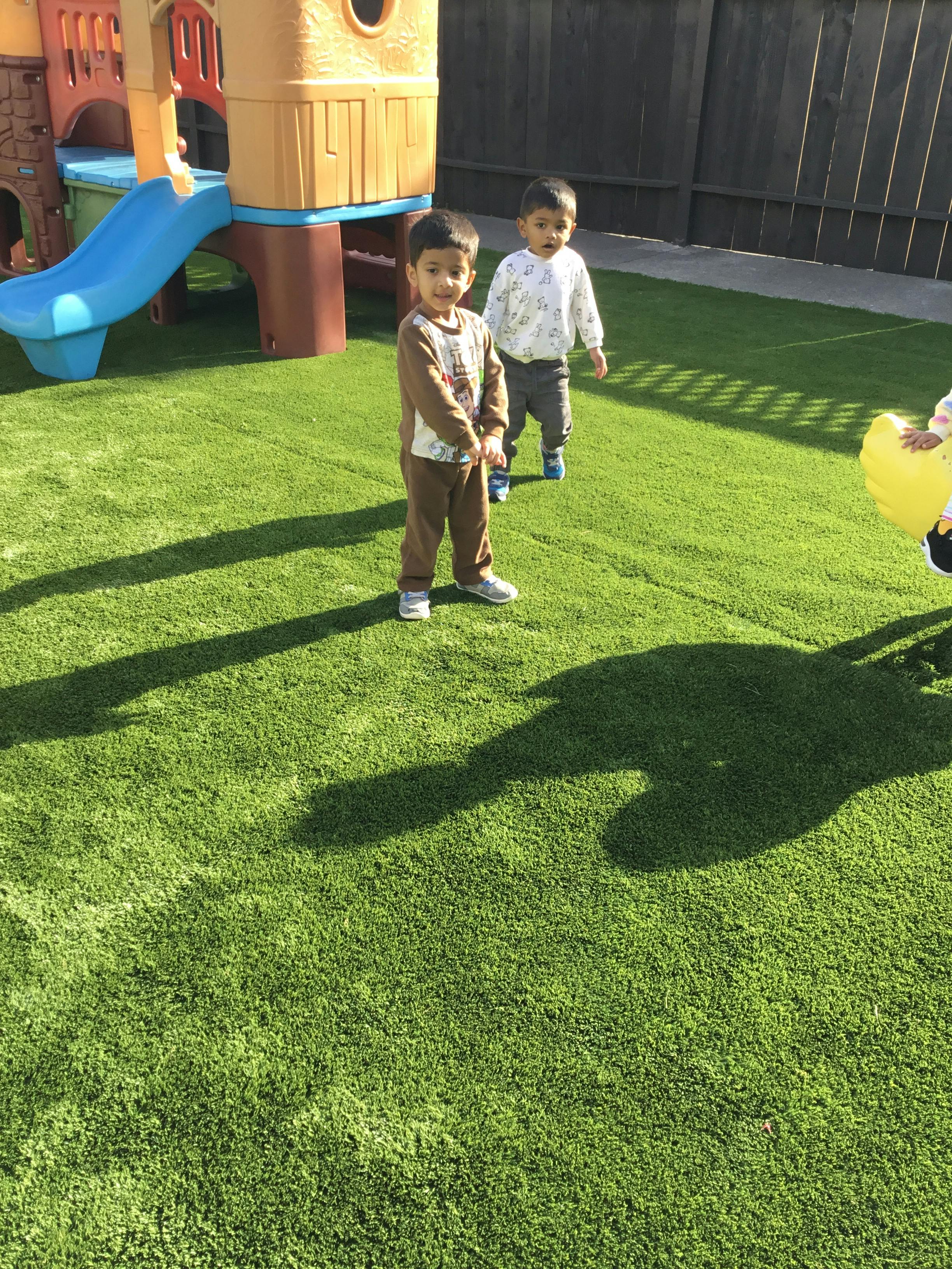 Two children standing on artificial grass next to a playground slide