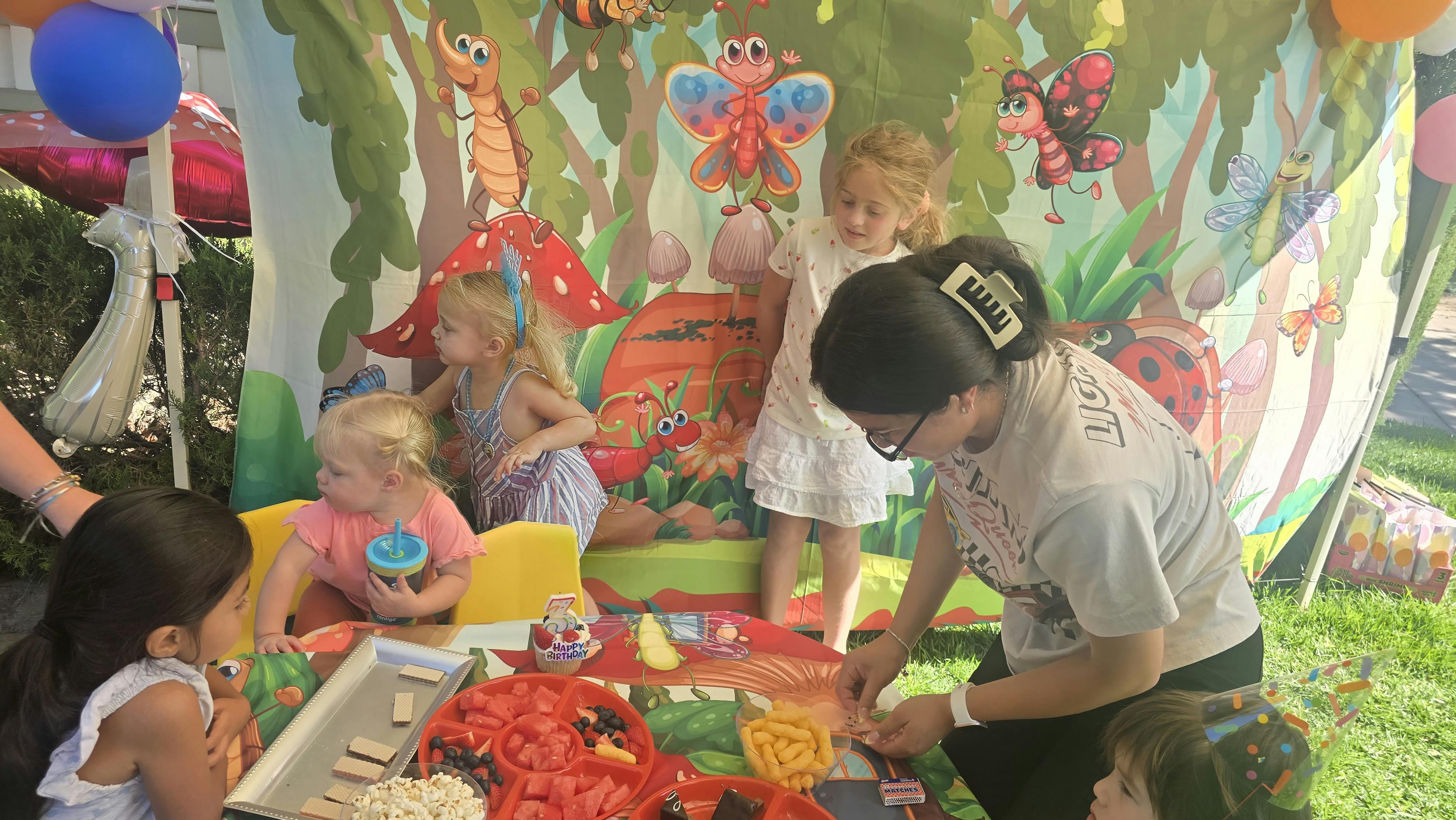 Group of children and a person near a birthday party table with snacks