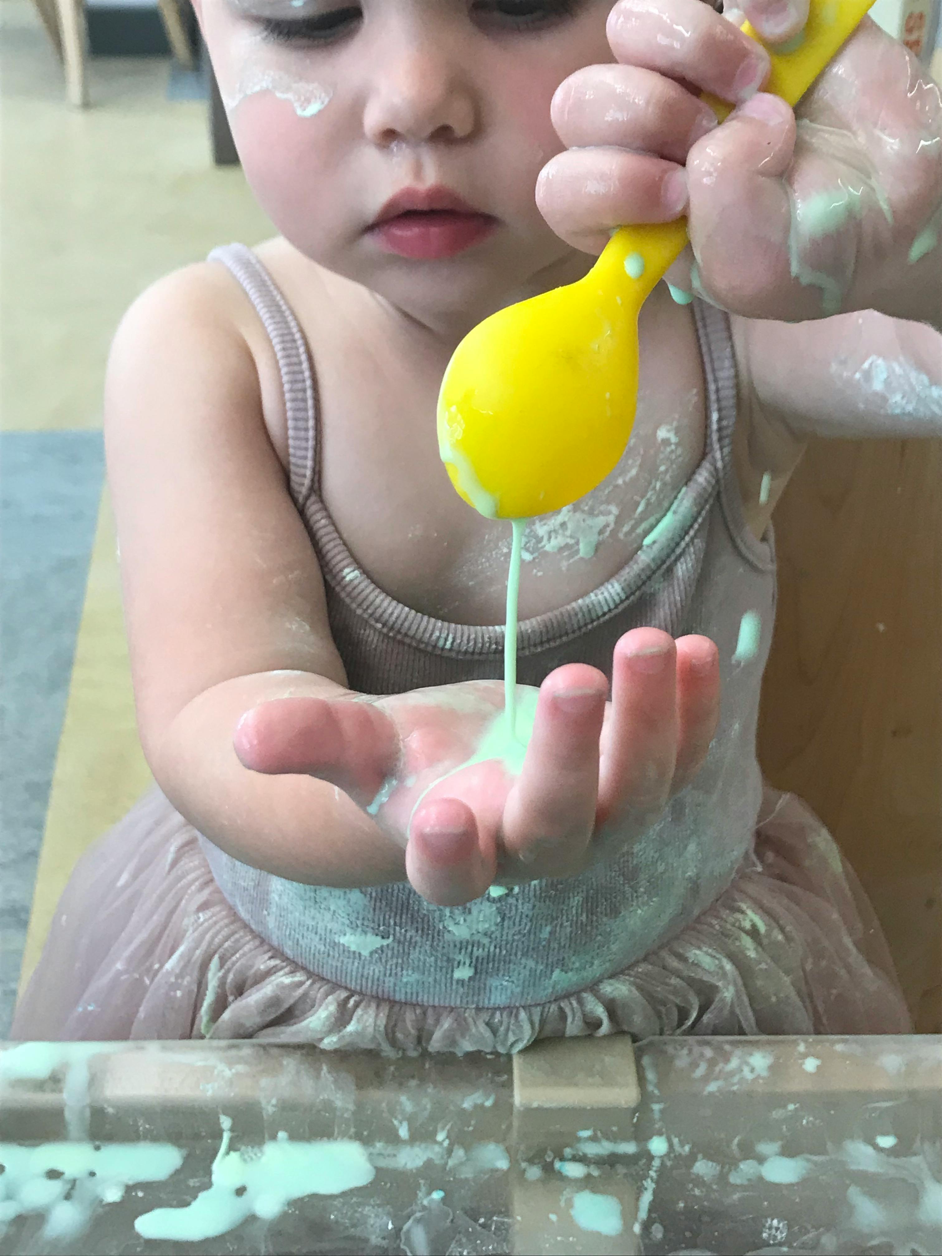 Child holding a yellow spoon with green liquid dripping into their hand