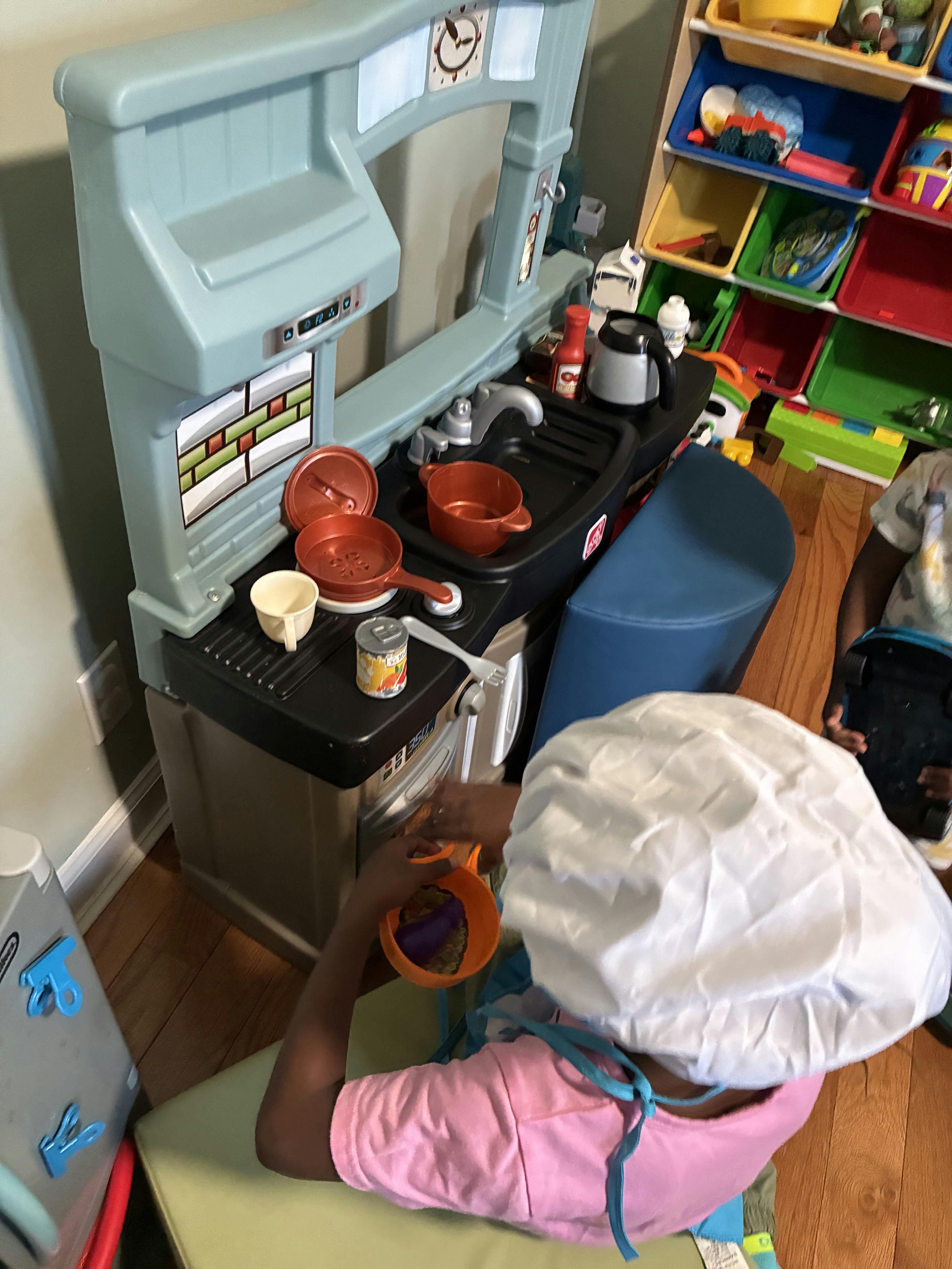 Child in a chef's hat playing with a toy kitchen
