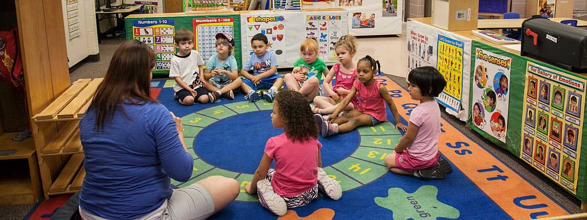 Adult and children sitting in a circle on a rug in a classroom