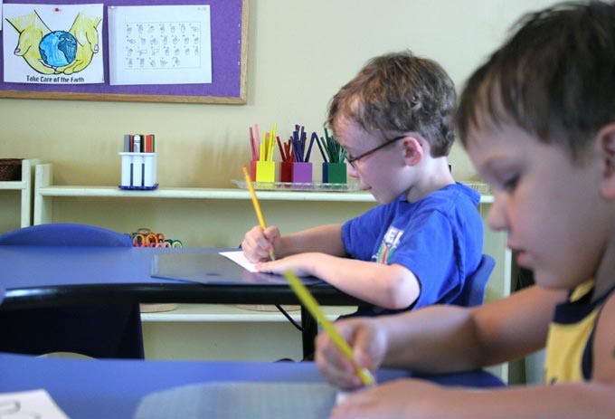 Two children drawing at desks in a classroom