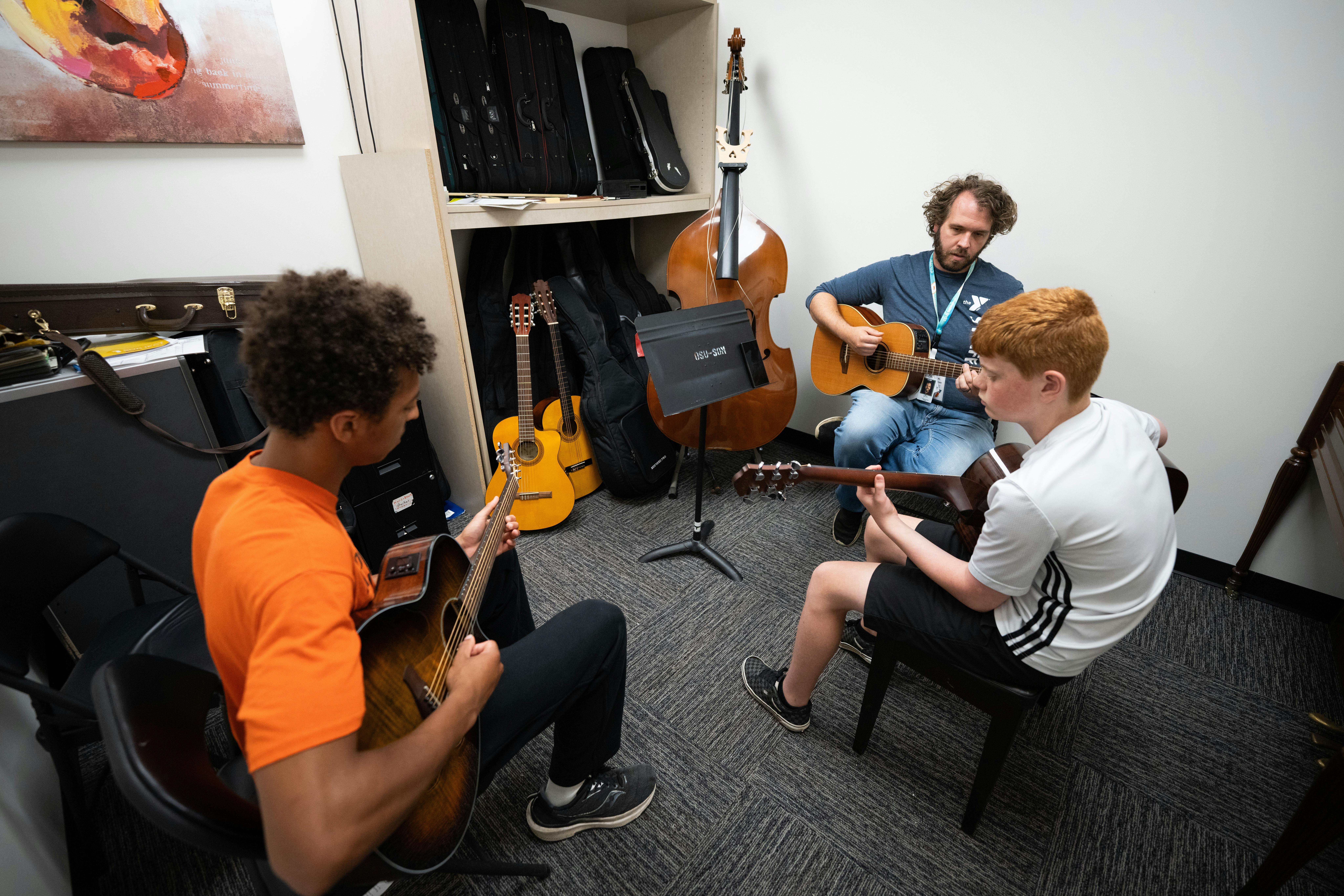 Adult and two teens playing guitars in a music room