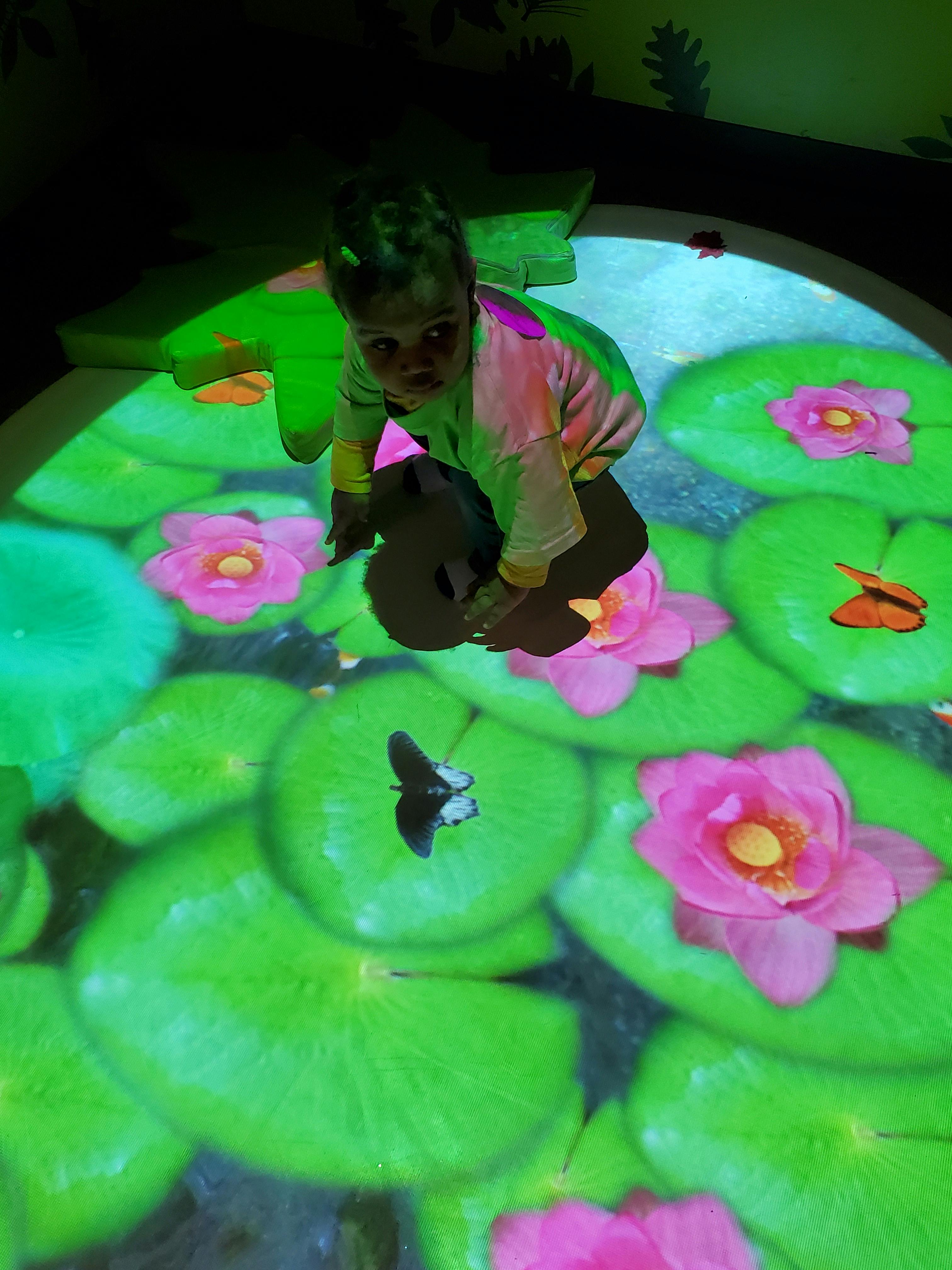 Child on hands and knees on a floor with projected lily pads and flowers