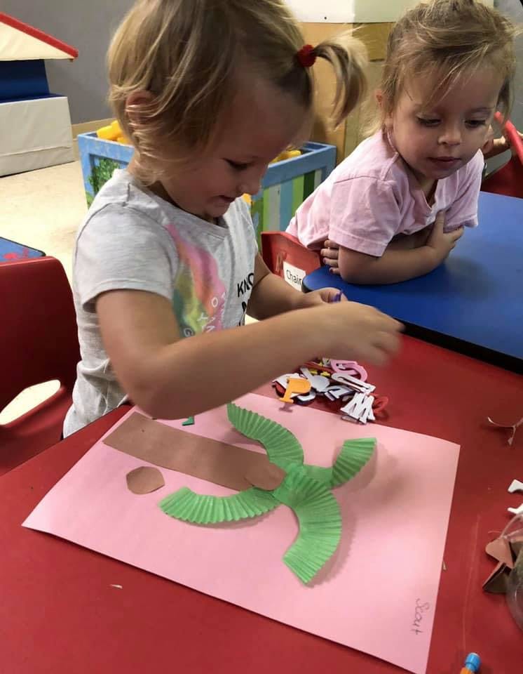Child making a craft with green paper on a pink sheet