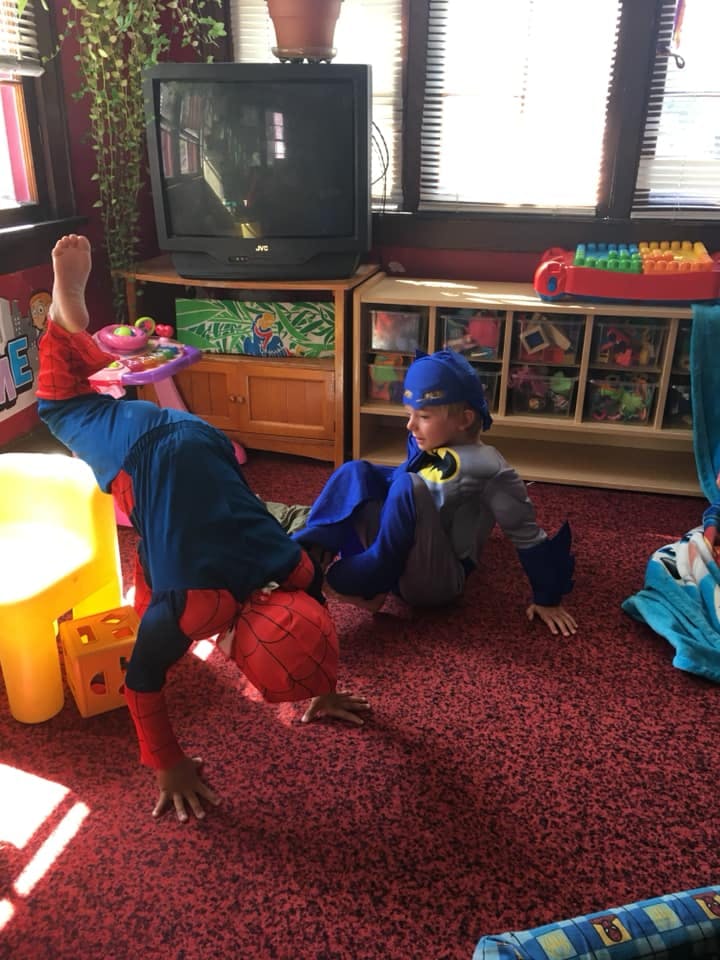 Child in Spider-Man costume doing a handstand next to a child in a Batman costume