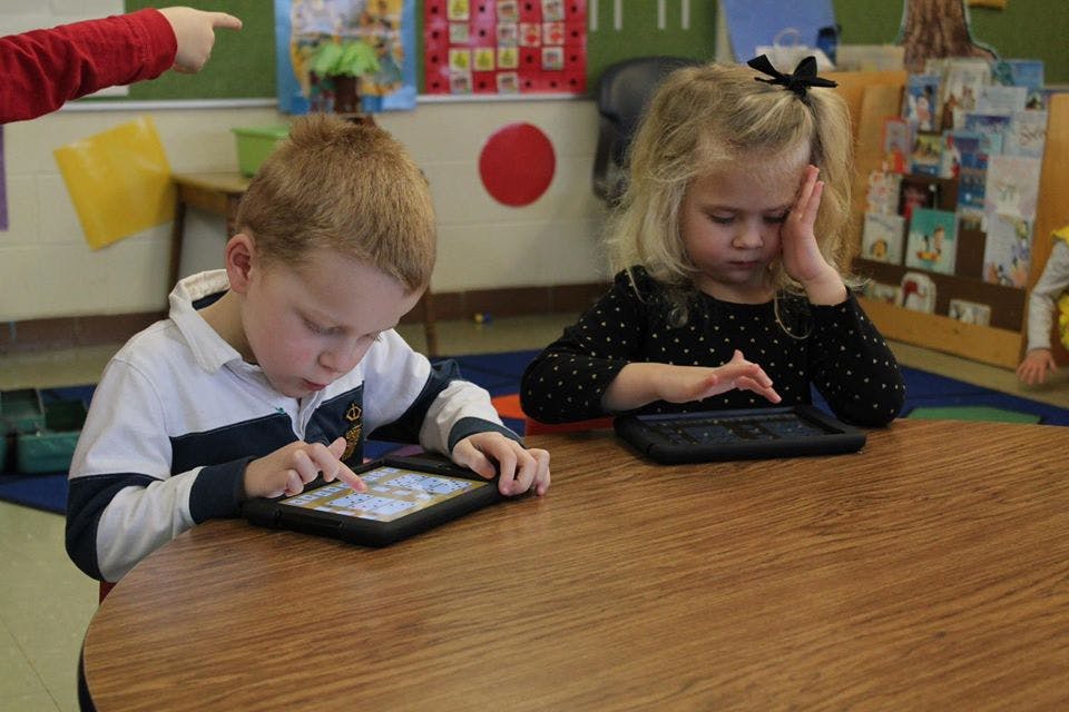Two children using tablets at a table in a classroom