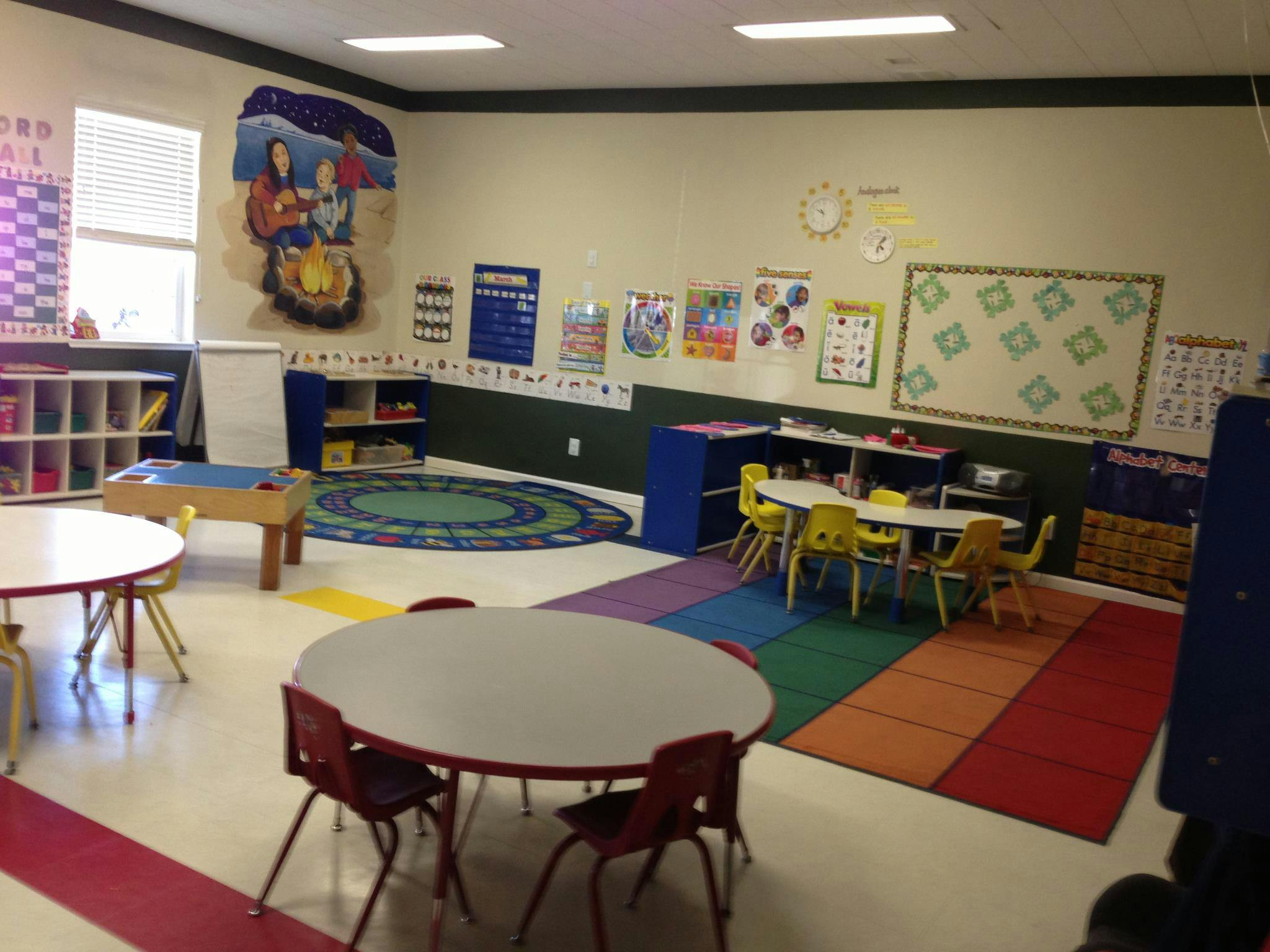 Classroom with small tables and chairs, colorful rugs, and wall decorations