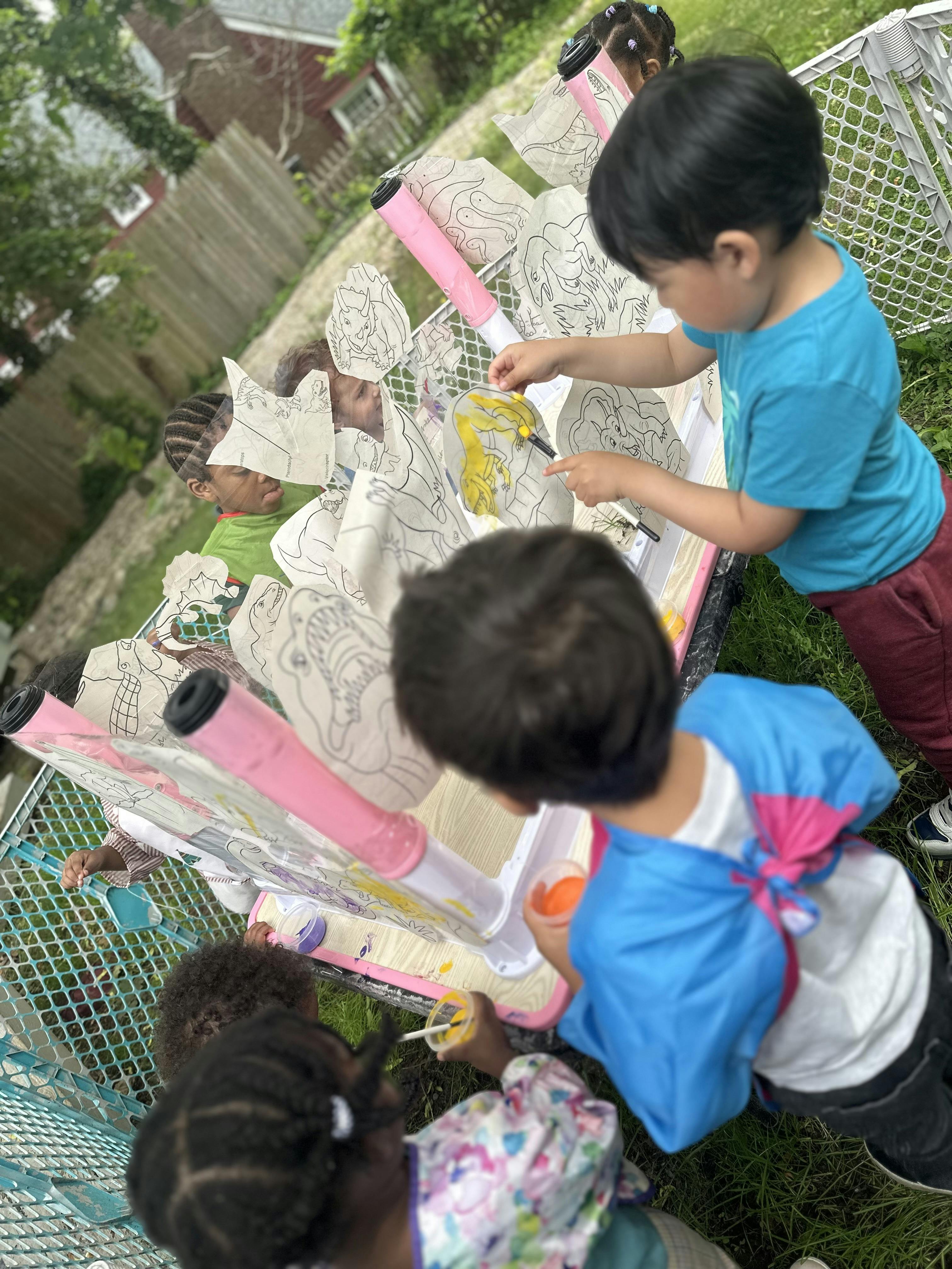Children painting paper cutouts outdoors