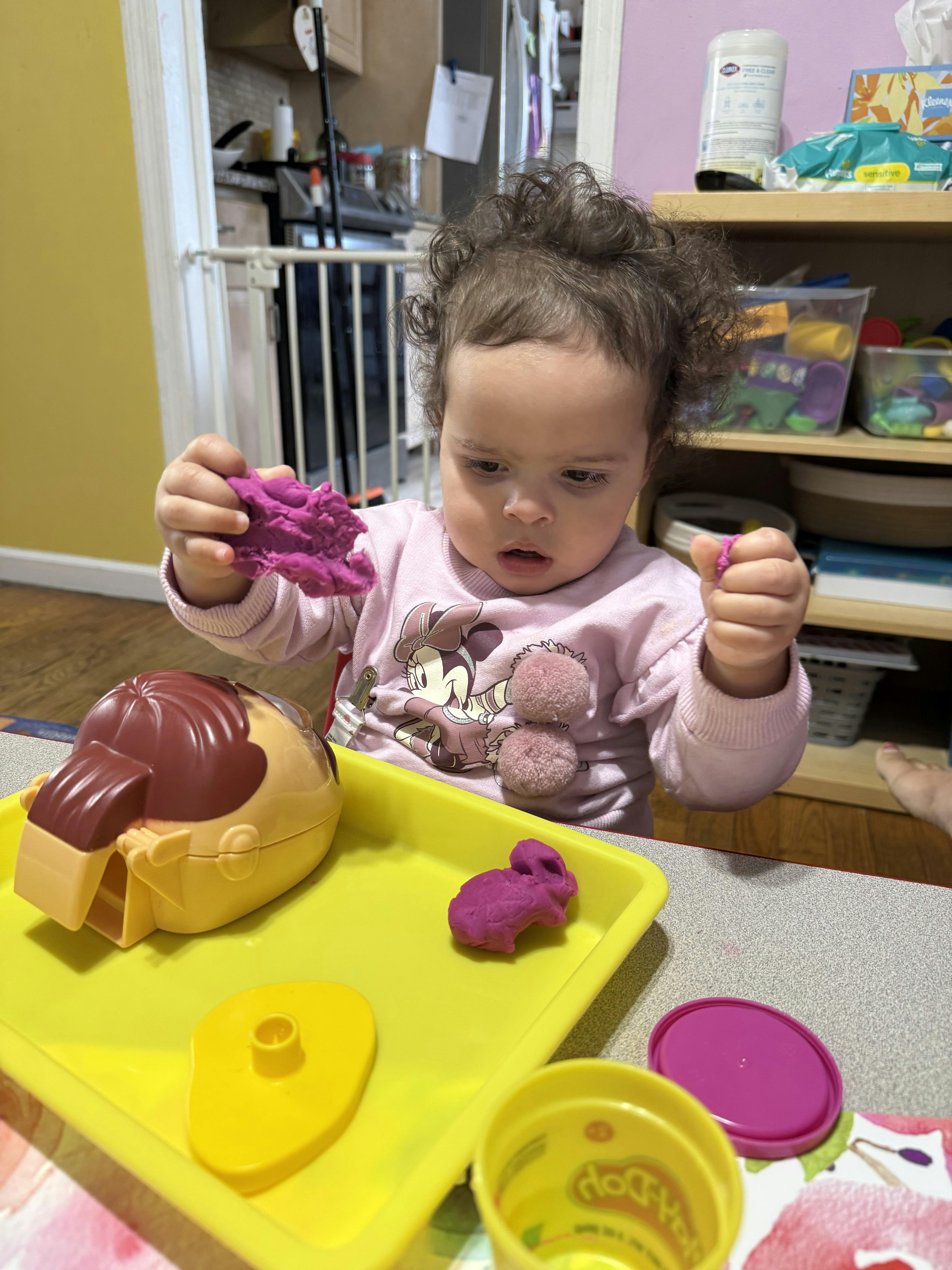 Child playing with purple modeling clay on a yellow tray
