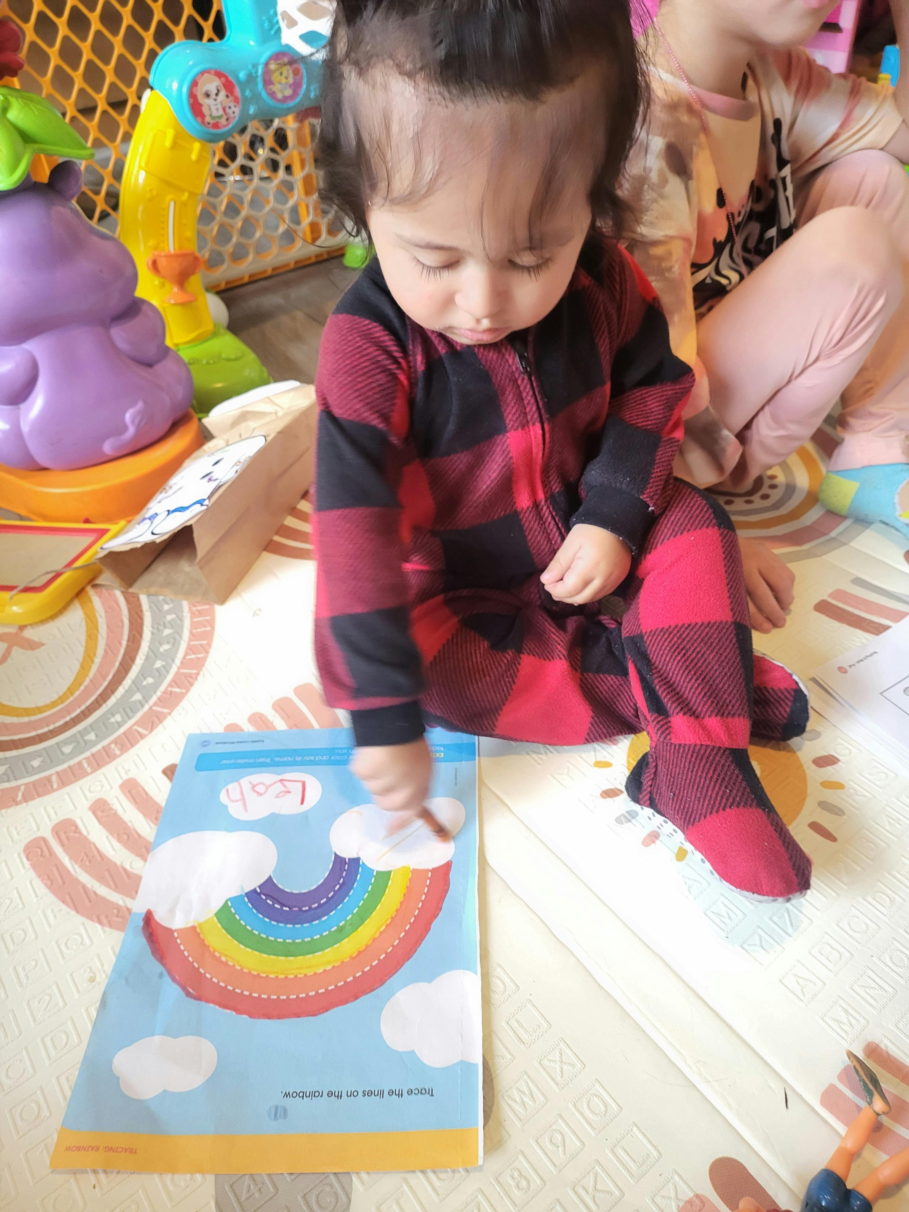 Child in plaid pajamas touching a rainbow picture