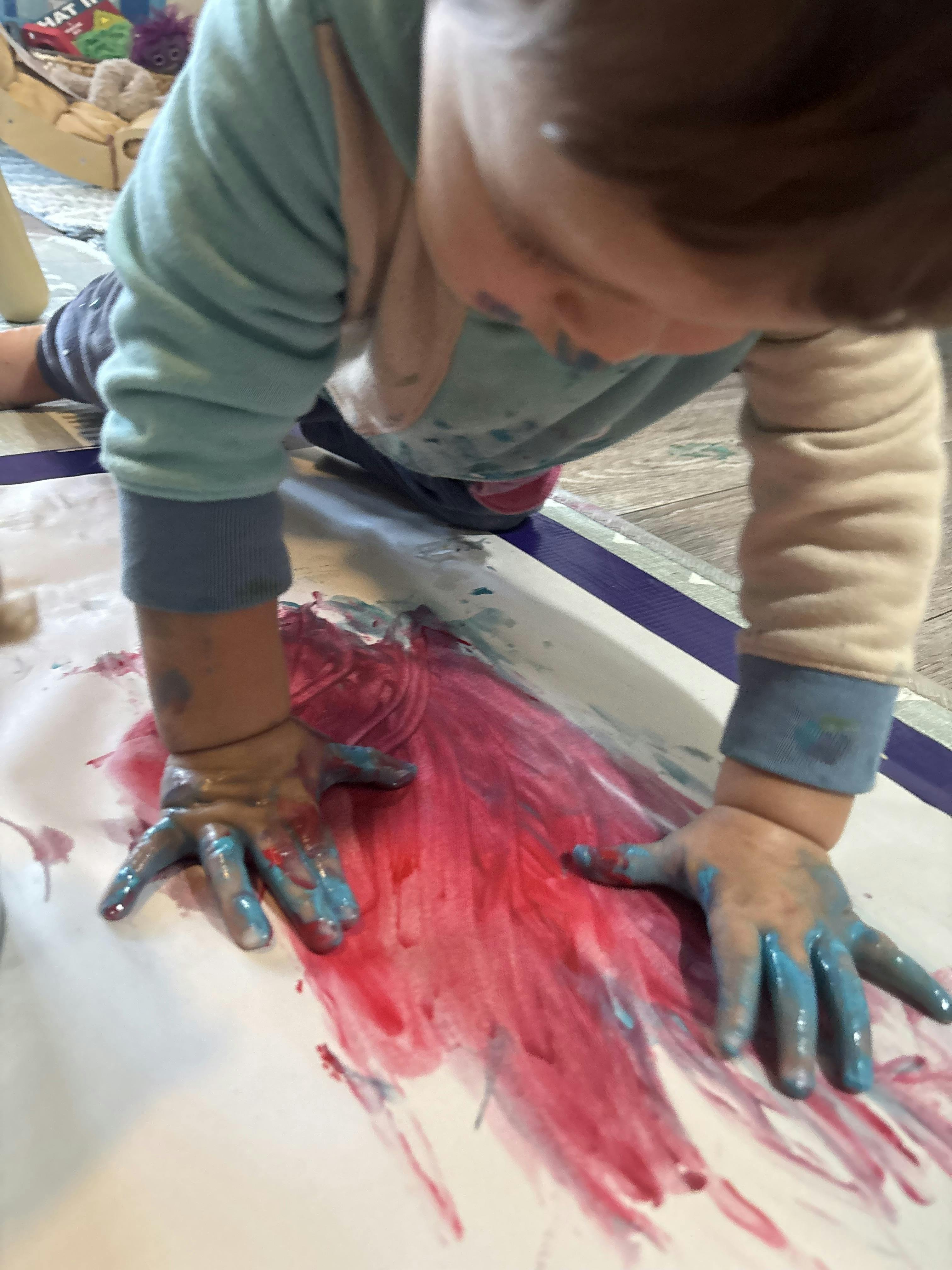 Child with hands covered in blue paint on paper with red paint