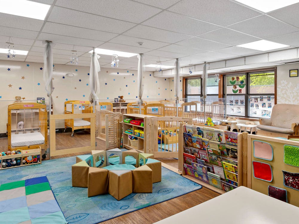 A brightly lit nursery room with multiple cribs, a reading nook, and play area