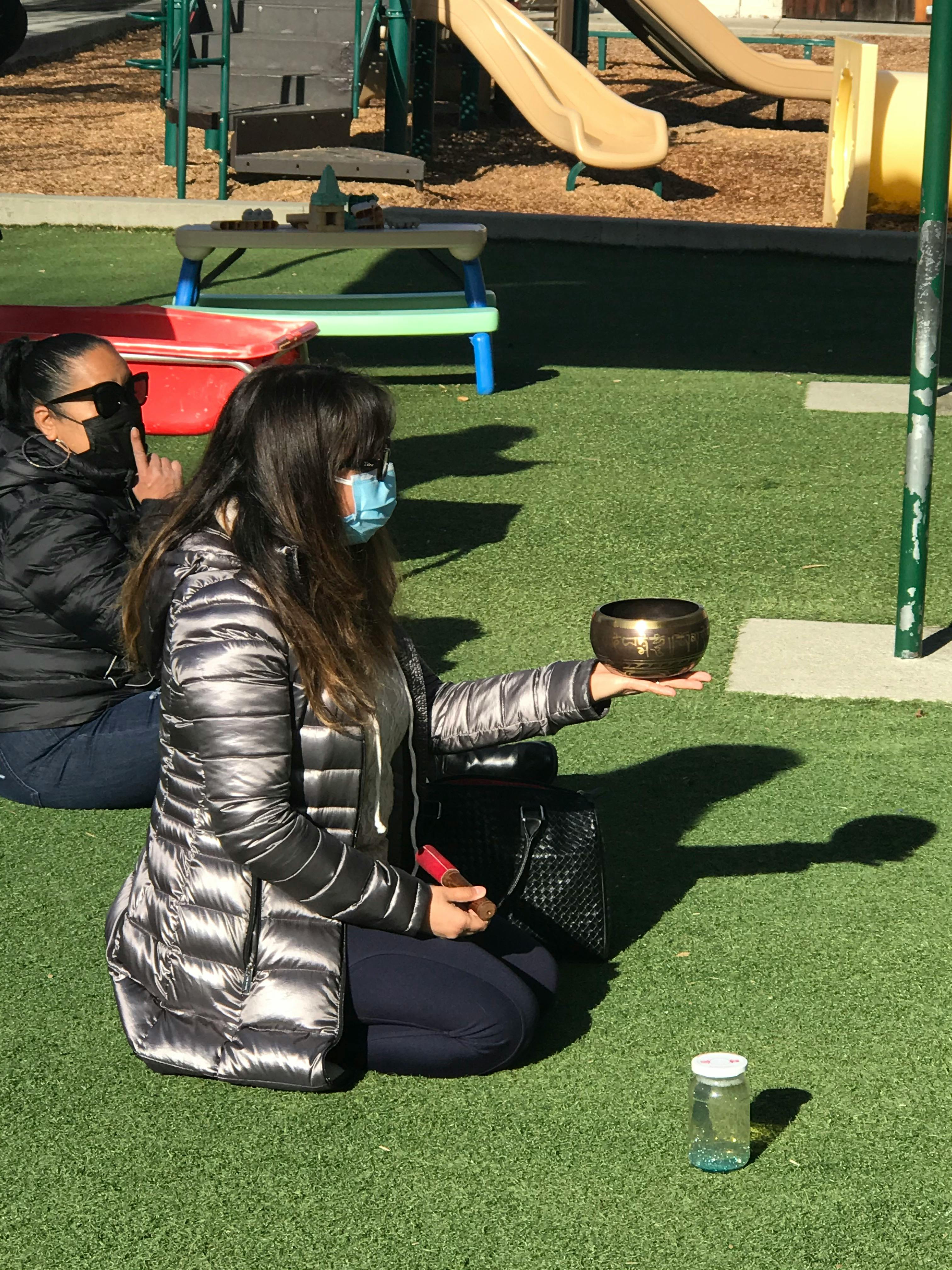 Person in face mask holding a small bowl while kneeling on artificial grass