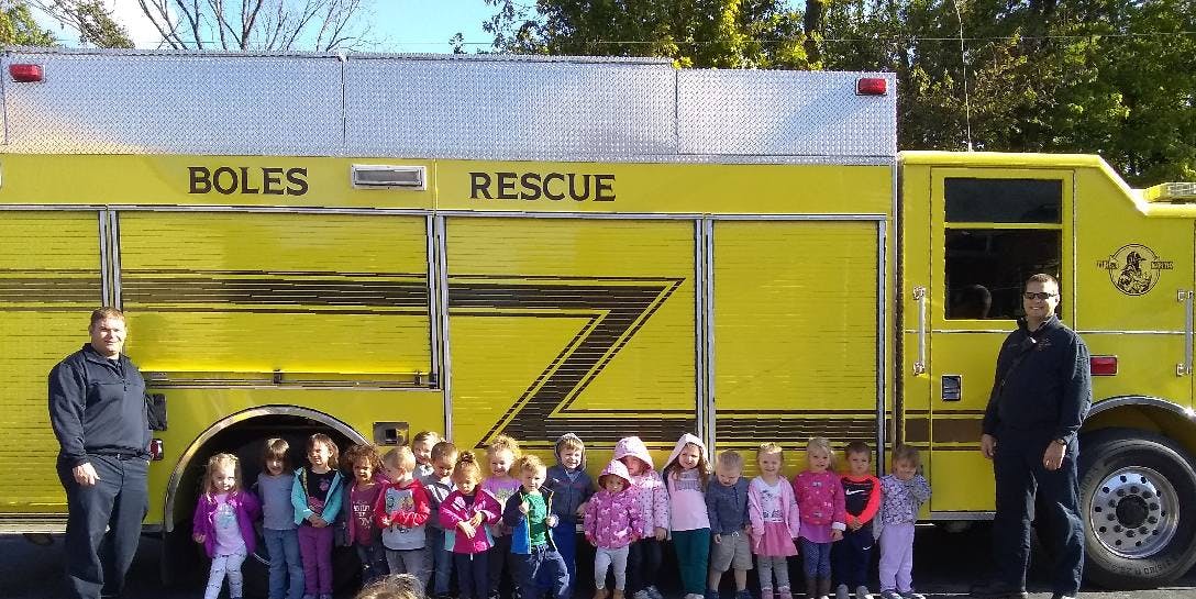Two people and a group of children standing in front of a yellow rescue truck