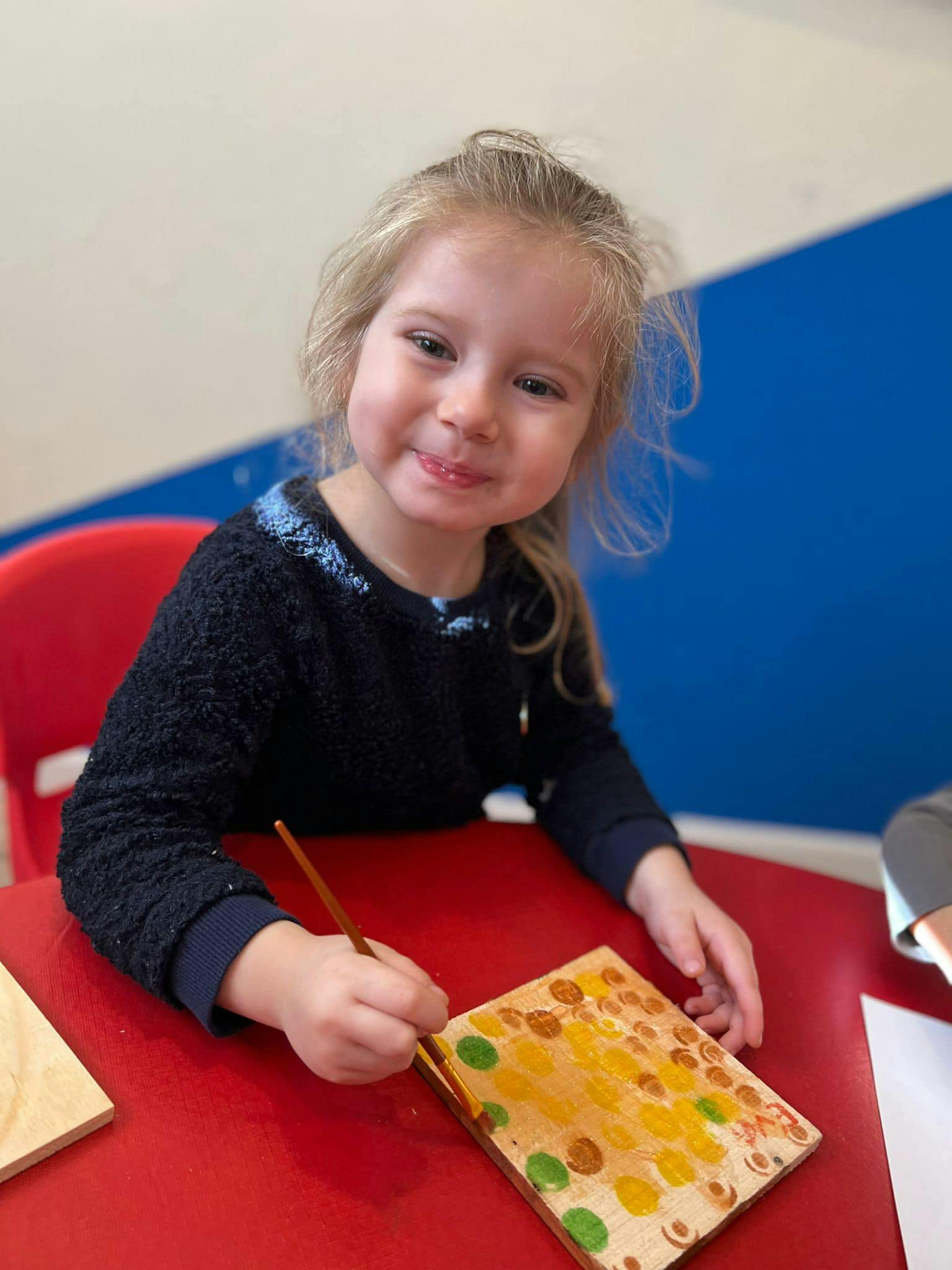 Child painting on a wooden board at a red table