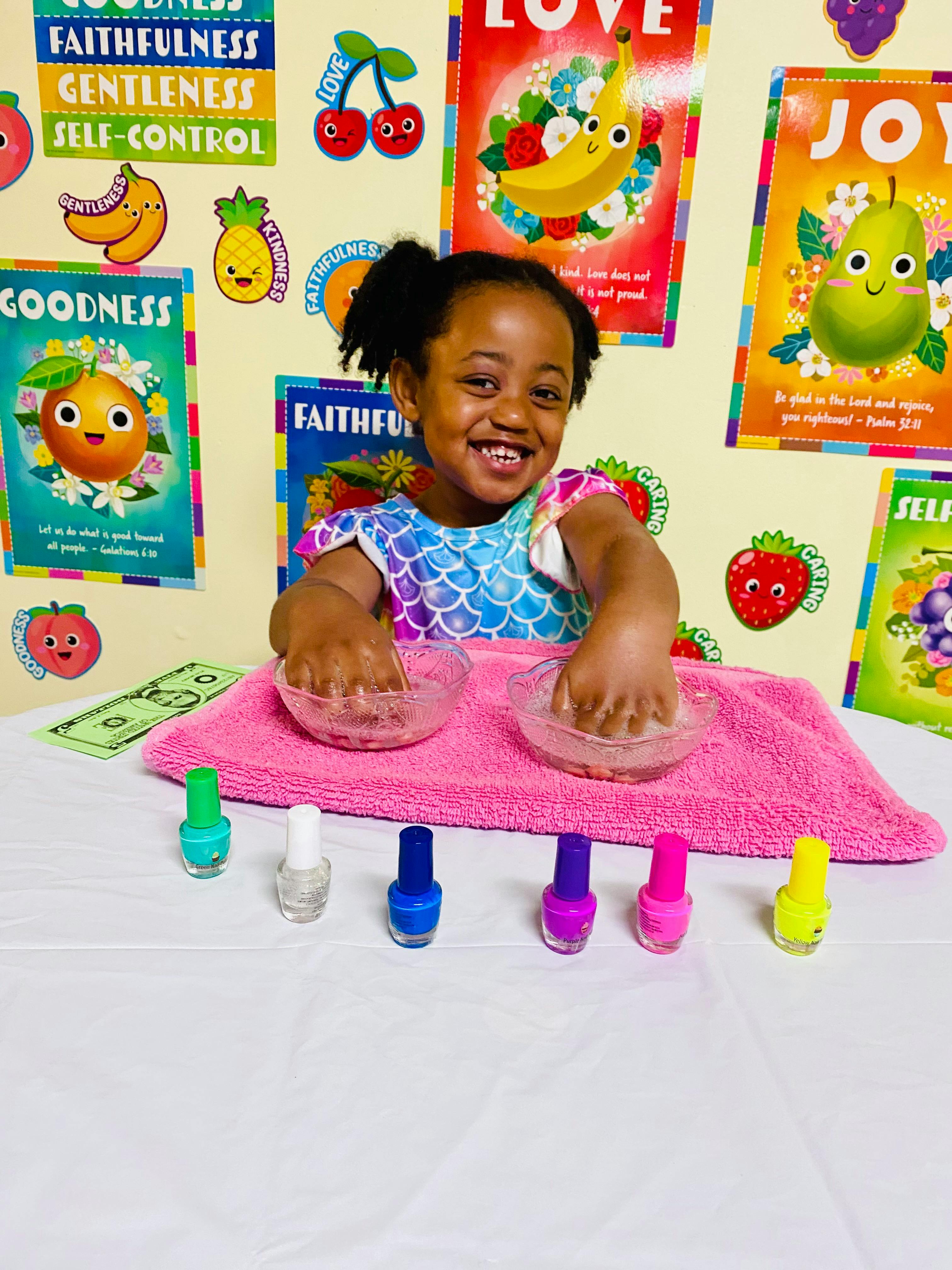 Child smiling while soaking hands in bowls with nail polish bottles nearby