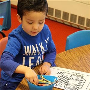 Child reaching into a bucket of crayons next to a coloring page