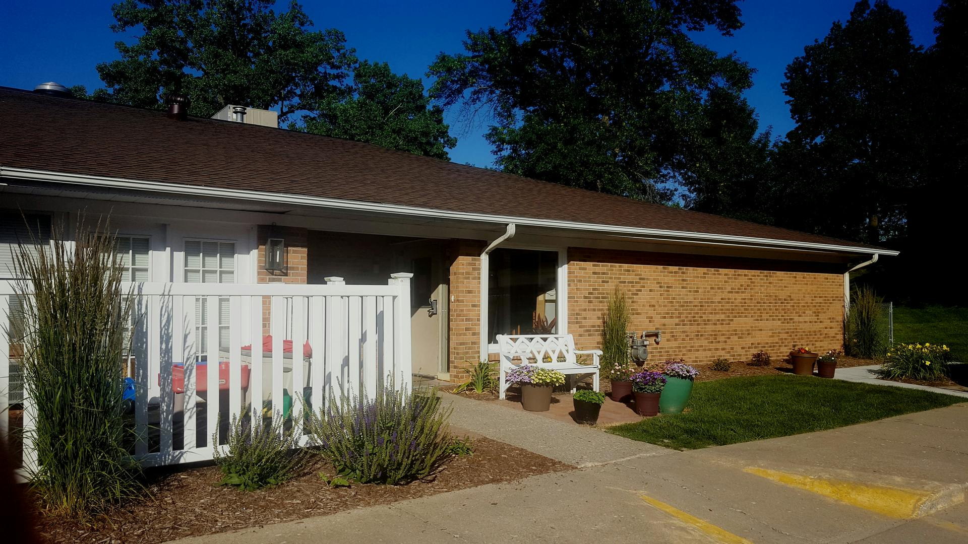 Exterior of a building with a brown roof and brick wall, white fence in front