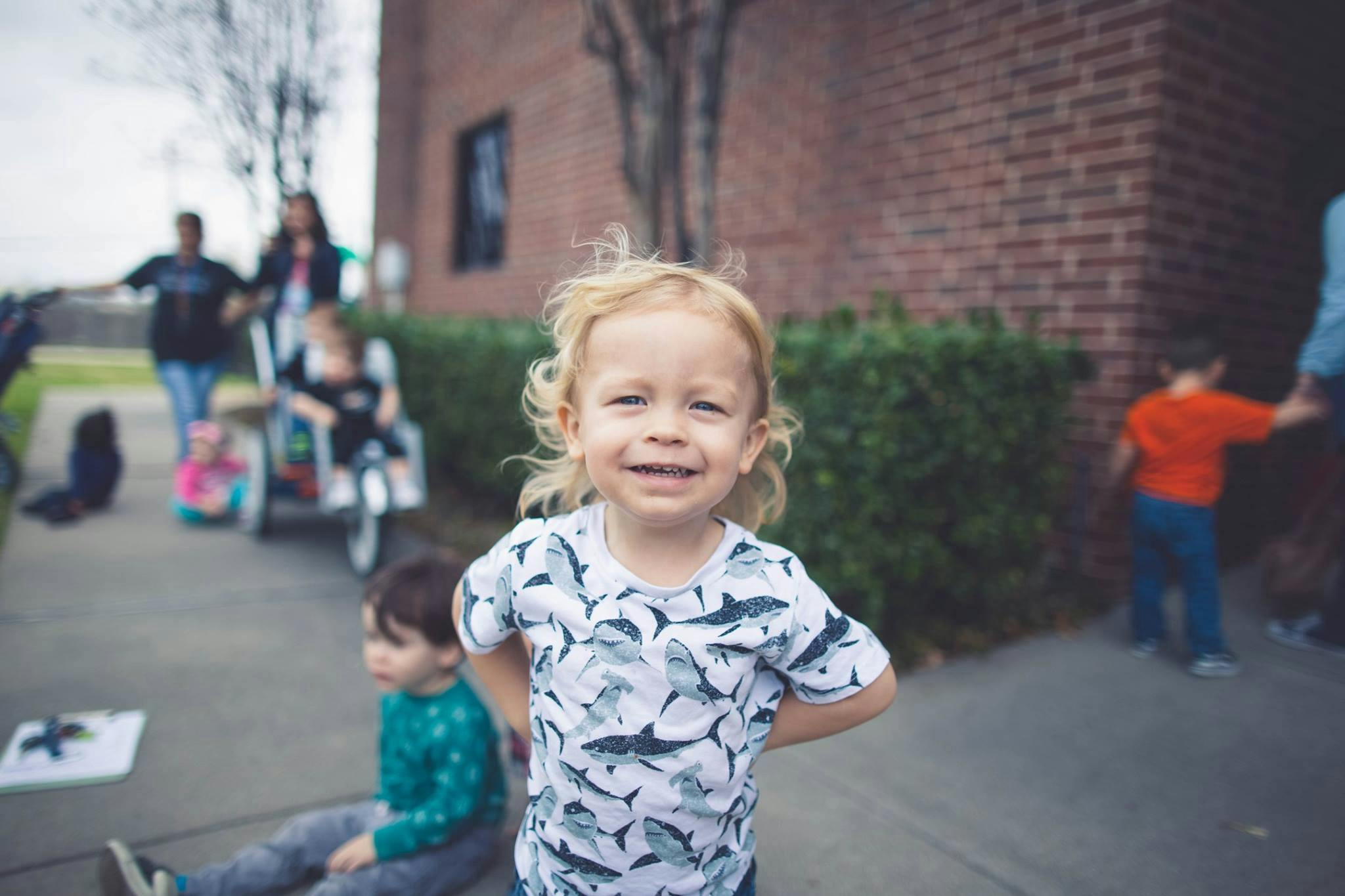 Child with curly hair smiling at camera, other children and adults in background