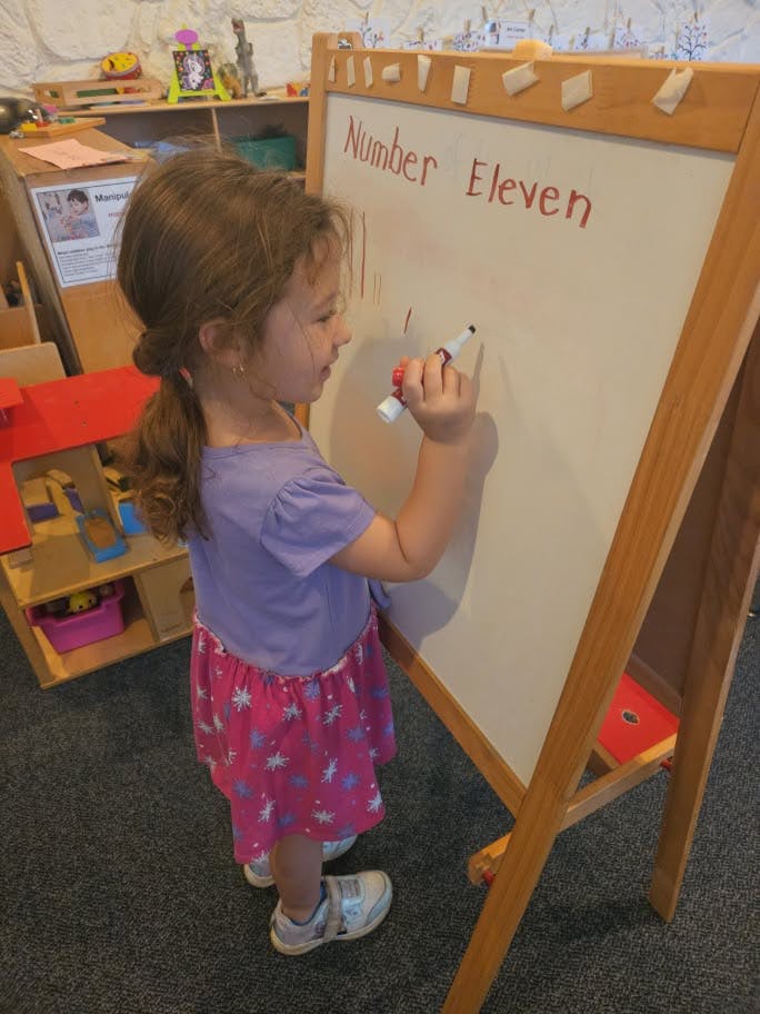 Child writing number eleven on a whiteboard in a classroom