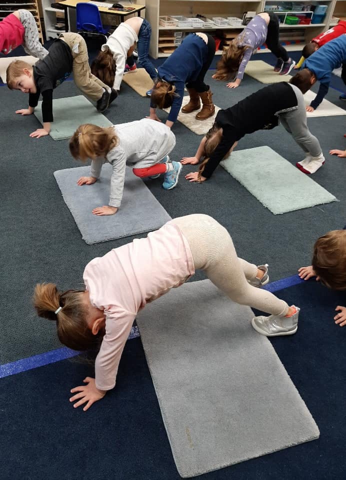 Children doing yoga poses on mats in a classroom