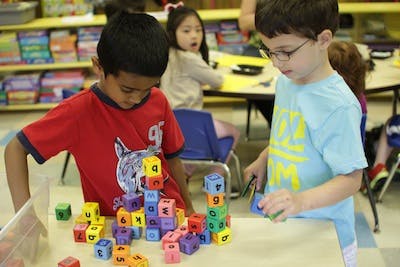 Two children playing with colorful alphabet blocks in a classroom
