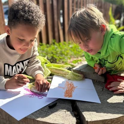 Two children drawing on paper outdoors