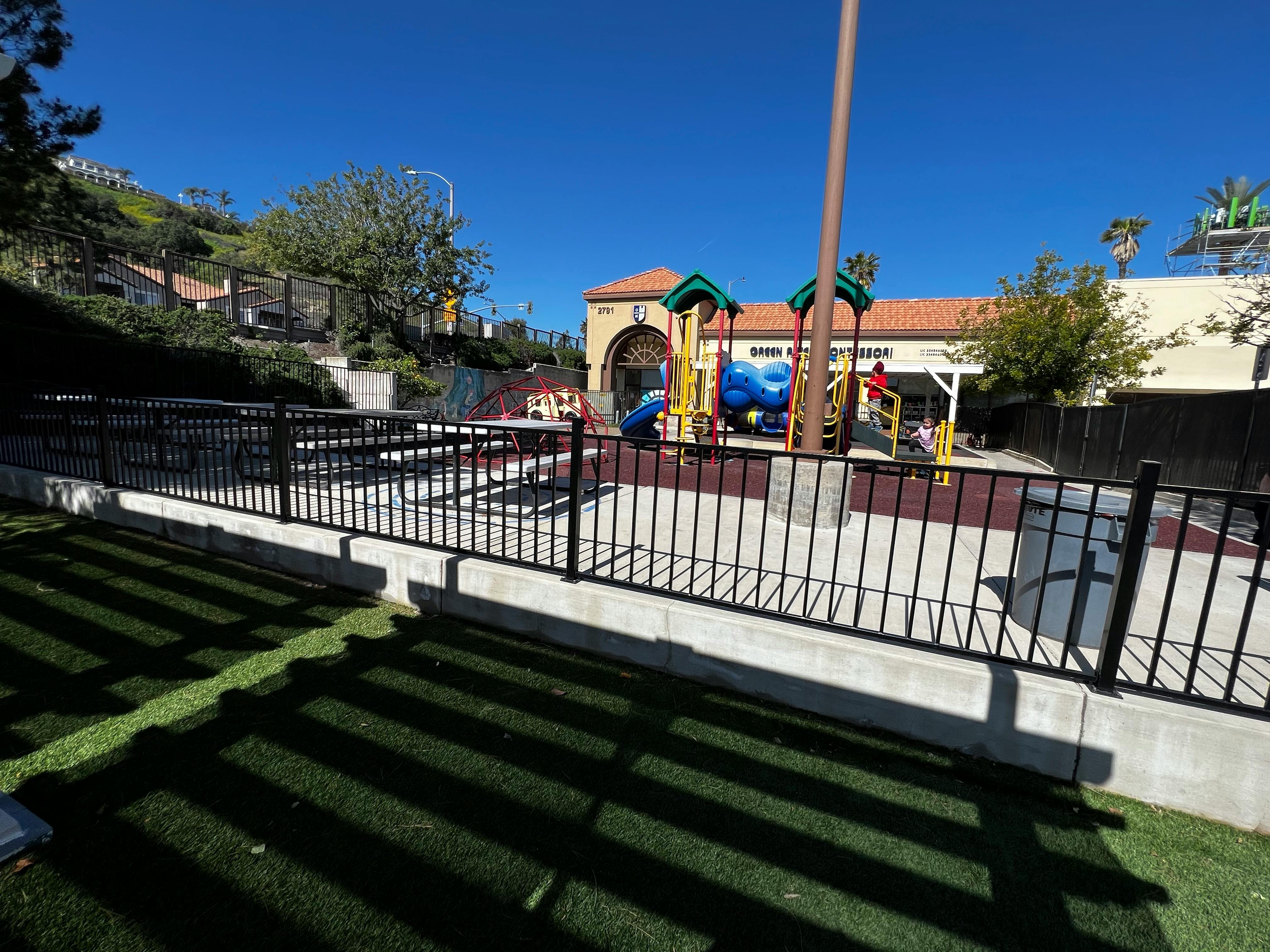 Outdoor playground with slides and climbing structures behind a black fence