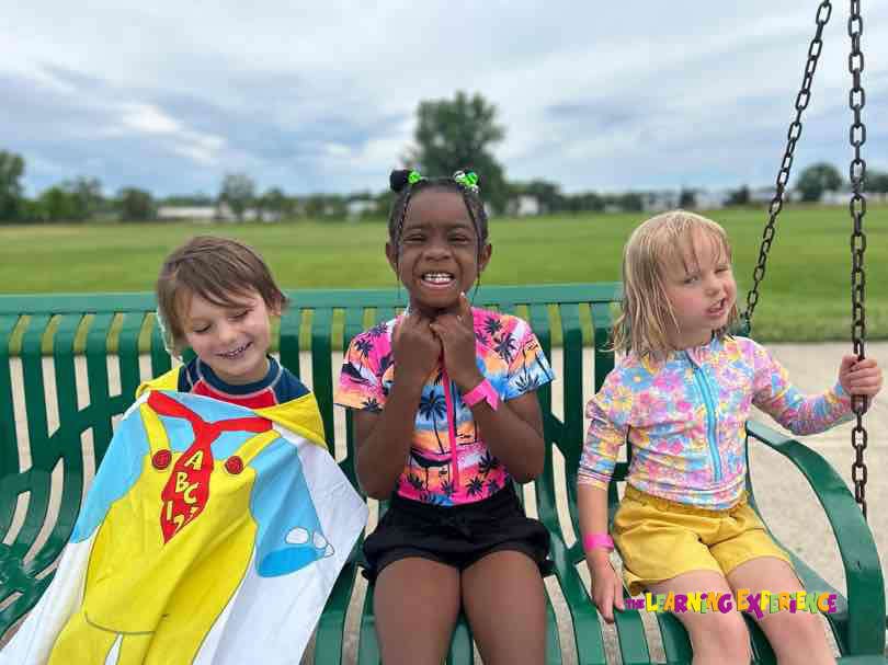 Three children sitting on a green bench swing
