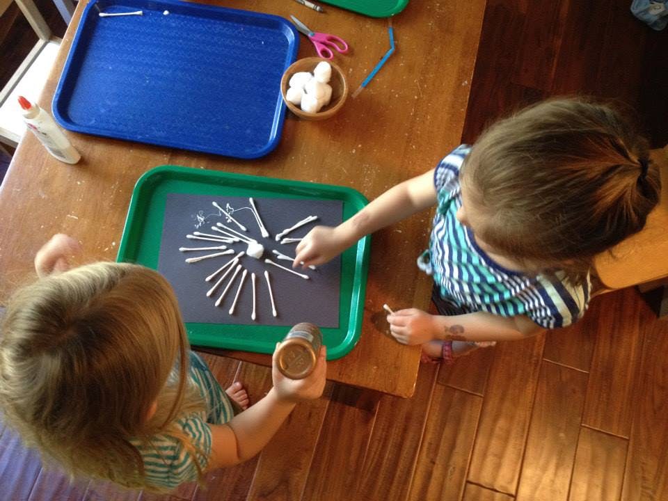 Two children playing with cotton swabs on a tray